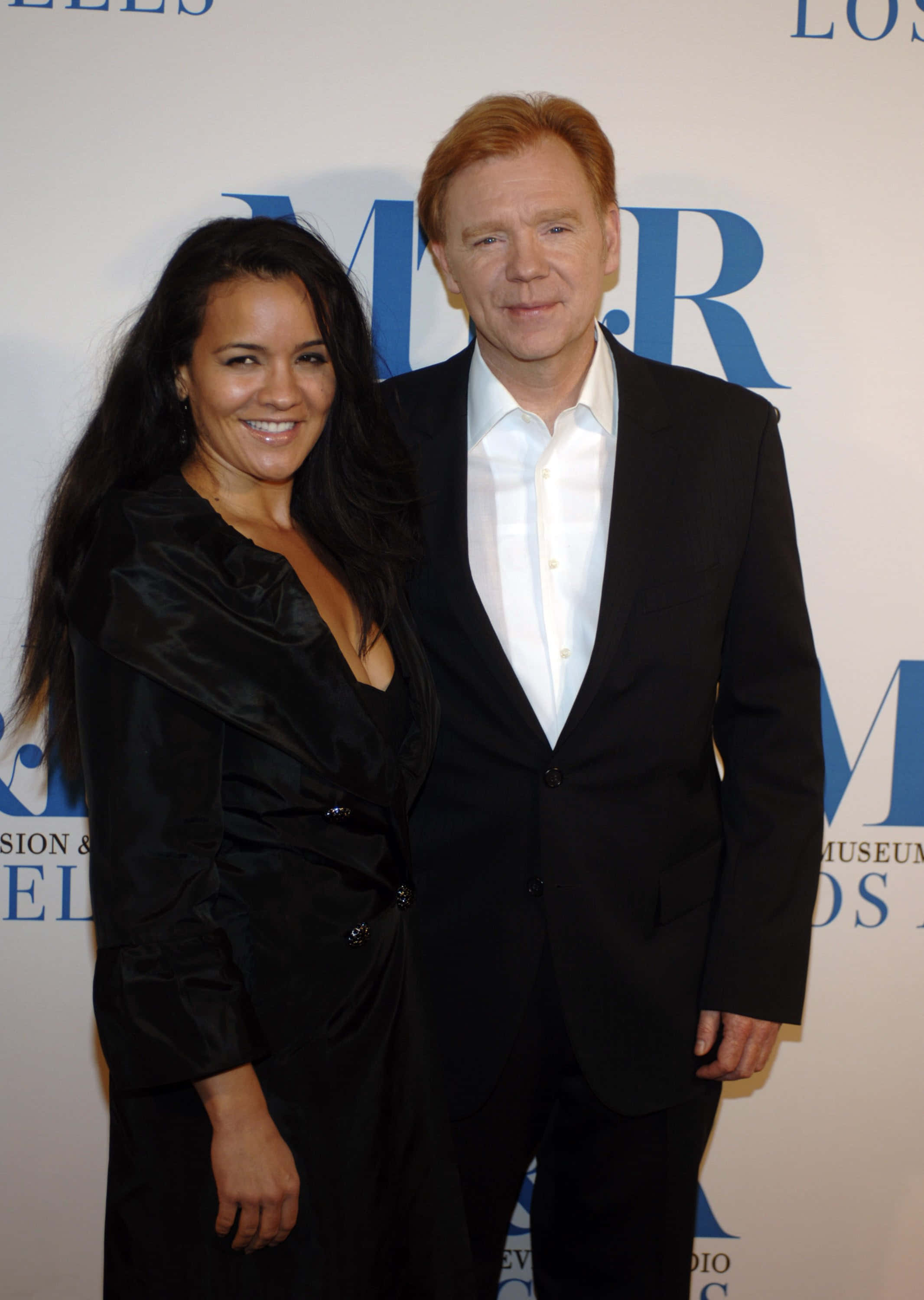 David Caruso 桌布 壁紙 — 一位微笑的男士和女士在品牌背景前於正式活動中一起擺姿勢。