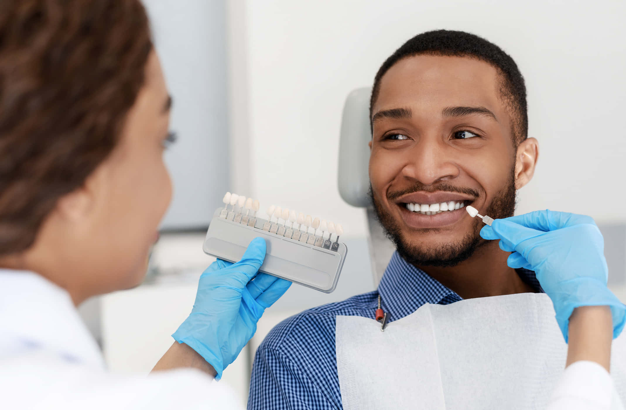 Teeth Whitening 桌布 壁紙 — 一位微笑的男士坐在牙科椅上，正接受牙醫手持色板進行牙齒美白治療。