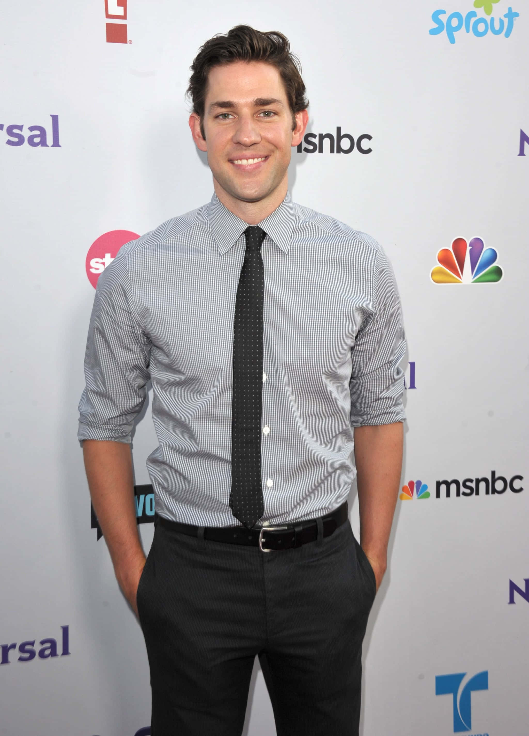 john krasinski 桌布 壁紙 — 一位微笑的男子穿著格仔襯衫和黑色領帶，自信地站在媒體活動中，身後有標誌。