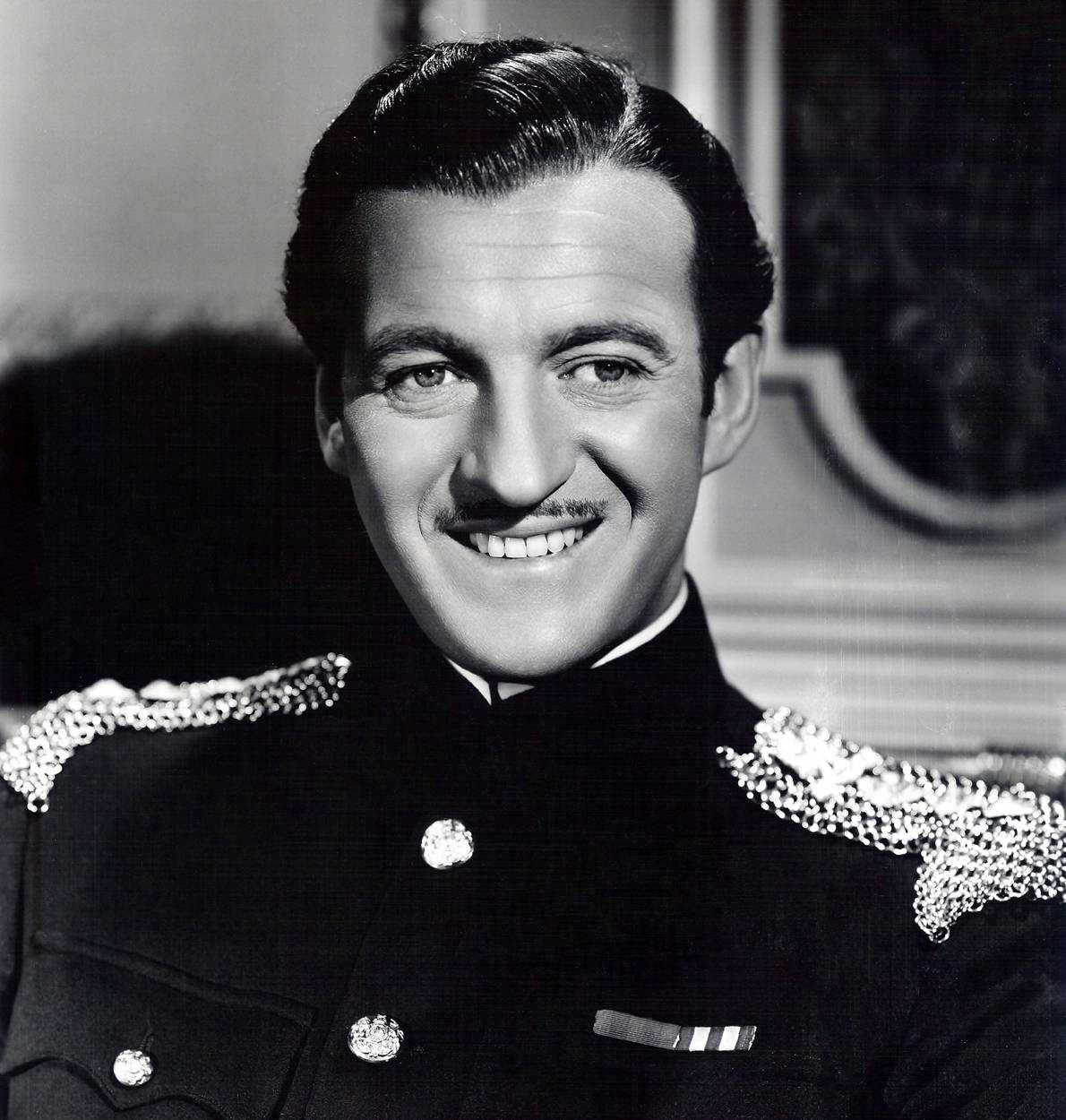 1948 Film Enchantment David Niven 壁紙 — 一位微笑的男子穿著正式軍裝，配有華麗的肩章和勳章，擺出經典黑白肖像姿勢。