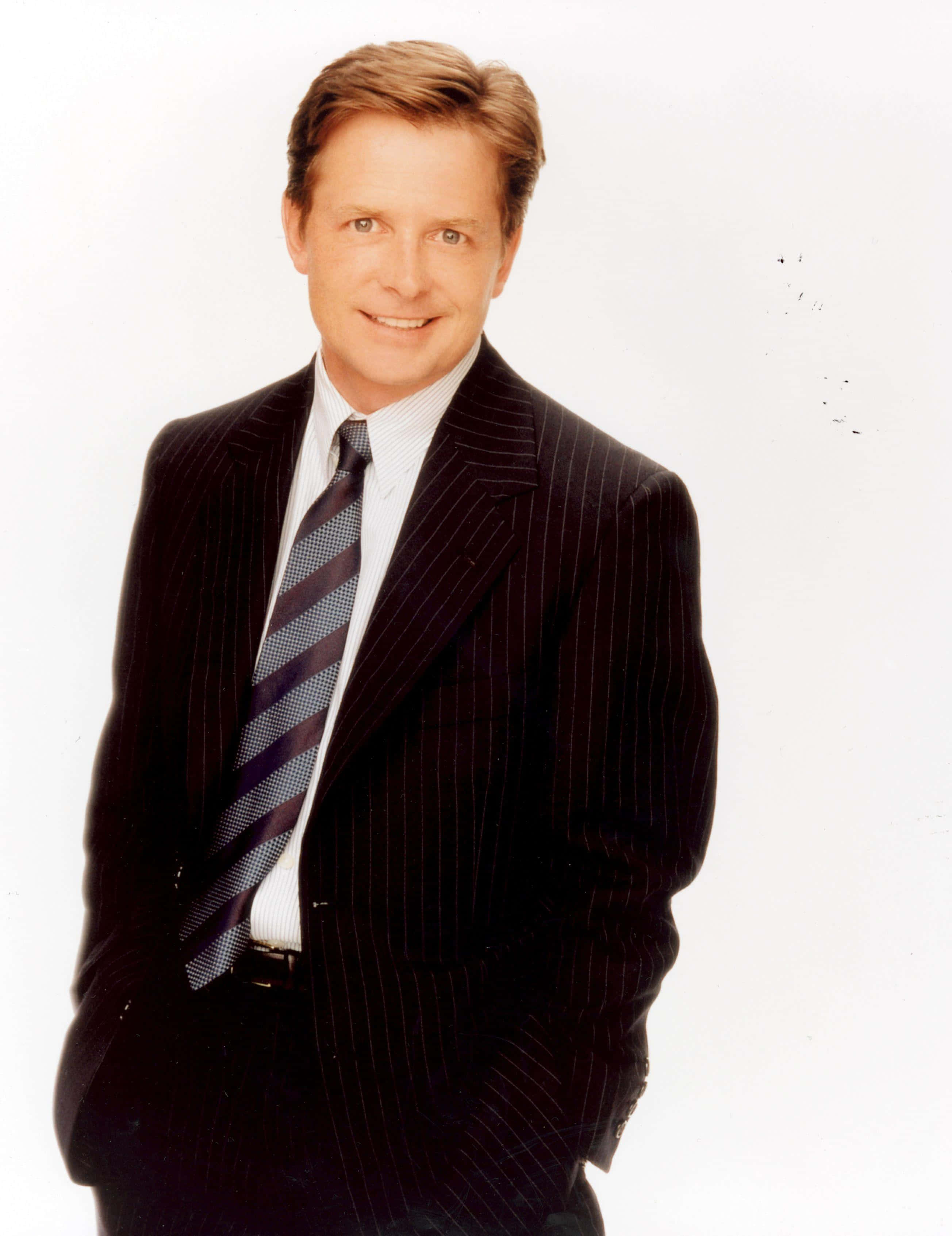 michael j fox 桌布 壁紙 — 一位微笑的男子穿著深色細條紋西裝和條紋領帶，在純白色背景前自信地擺姿勢。