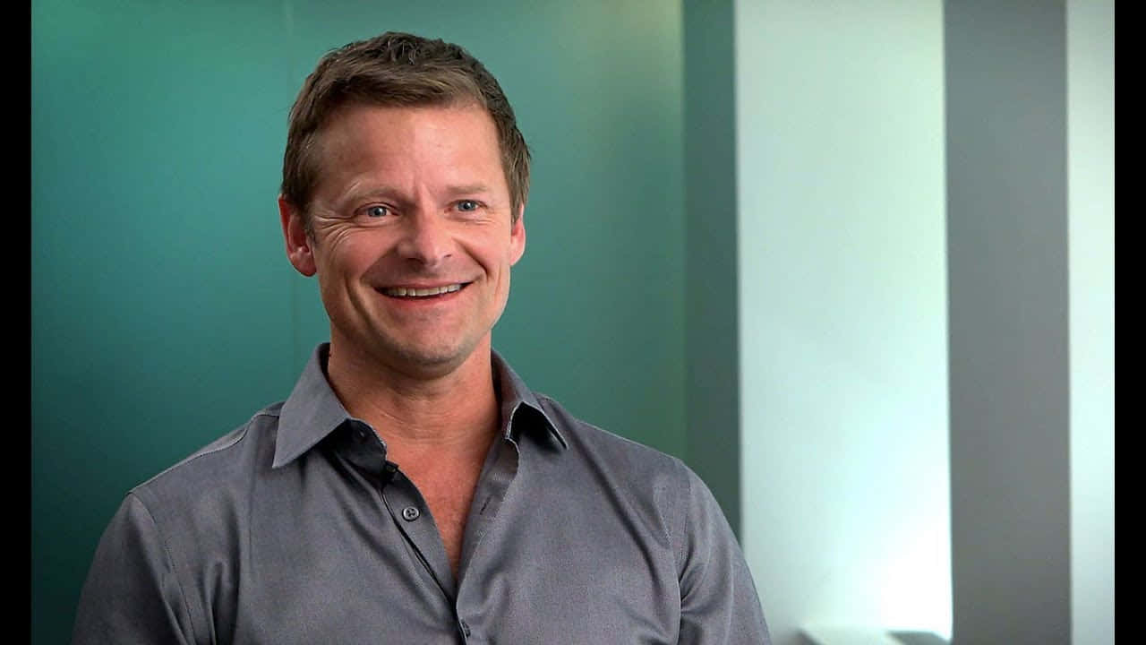 Steve Zahn 桌布 壁紙 — 一位微笑的男子穿著灰色襯衫，站在青綠色和白色條紋的背景前，光線柔和。