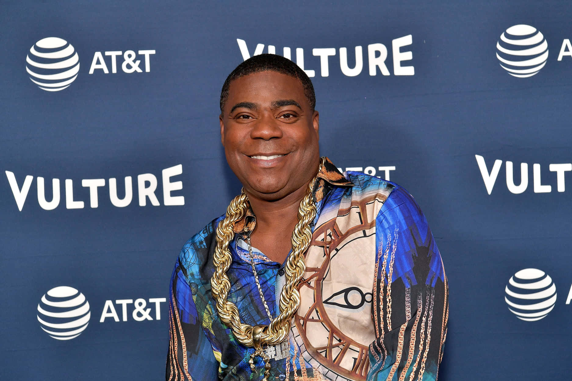 Tracy Morgan 桌布 壁紙 — 一位微笑的男子身穿鮮豔圖案襯衫和粗金鏈，在藍色Vulture AT&T品牌背景前擺姿勢。