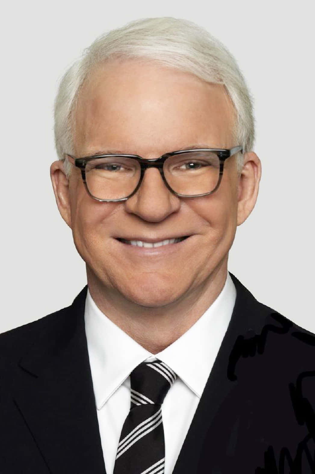 steve martin 桌布 壁紙 — 一位微笑的白髮男士戴著眼鏡，身穿黑色西裝和條紋領帶，背景為純灰色。