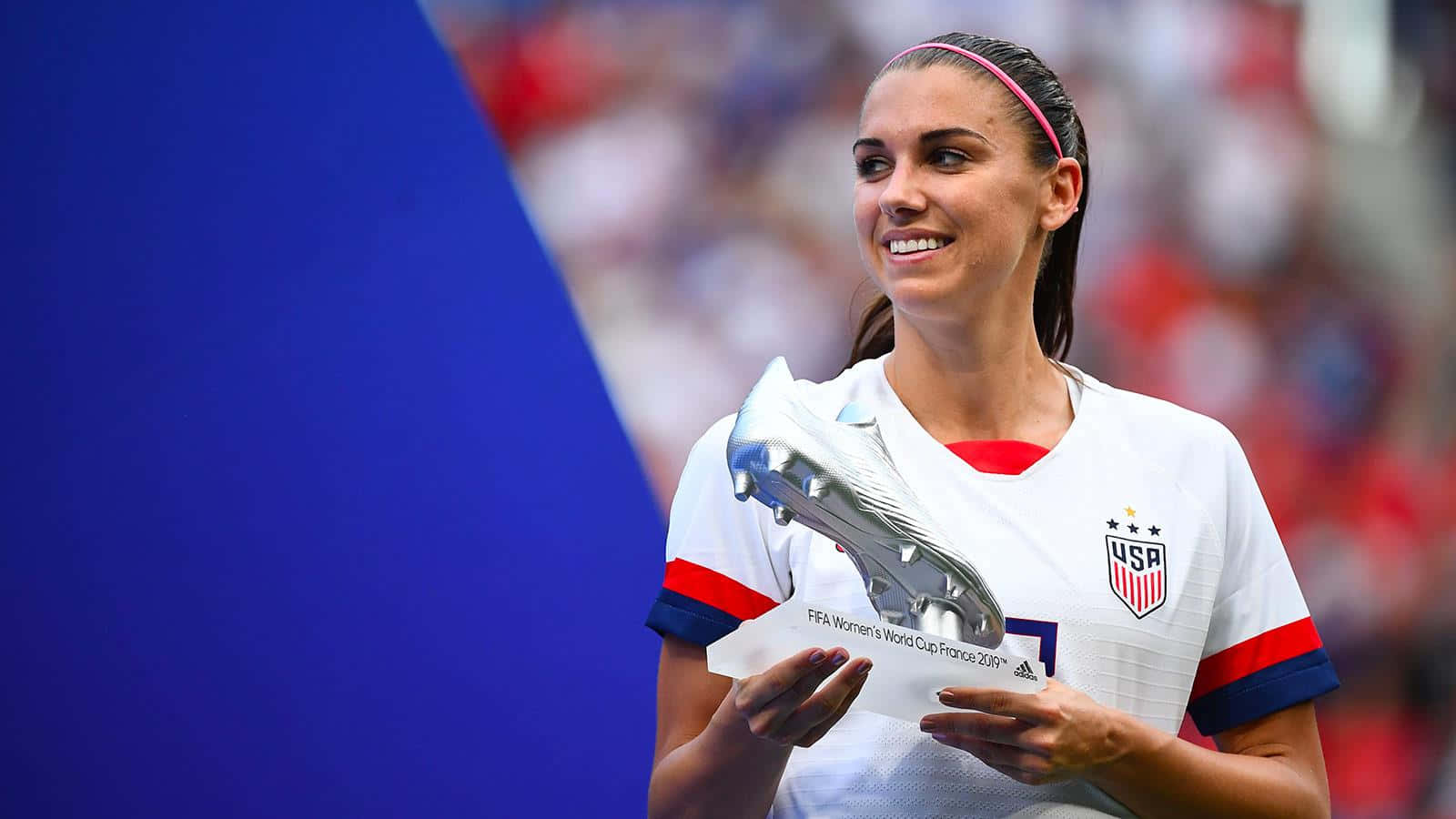Alex Morgan 桌布 壁紙 — 一位微笑的美國女足球員在2019年世界盃上自豪地捧起她的金靴獎。