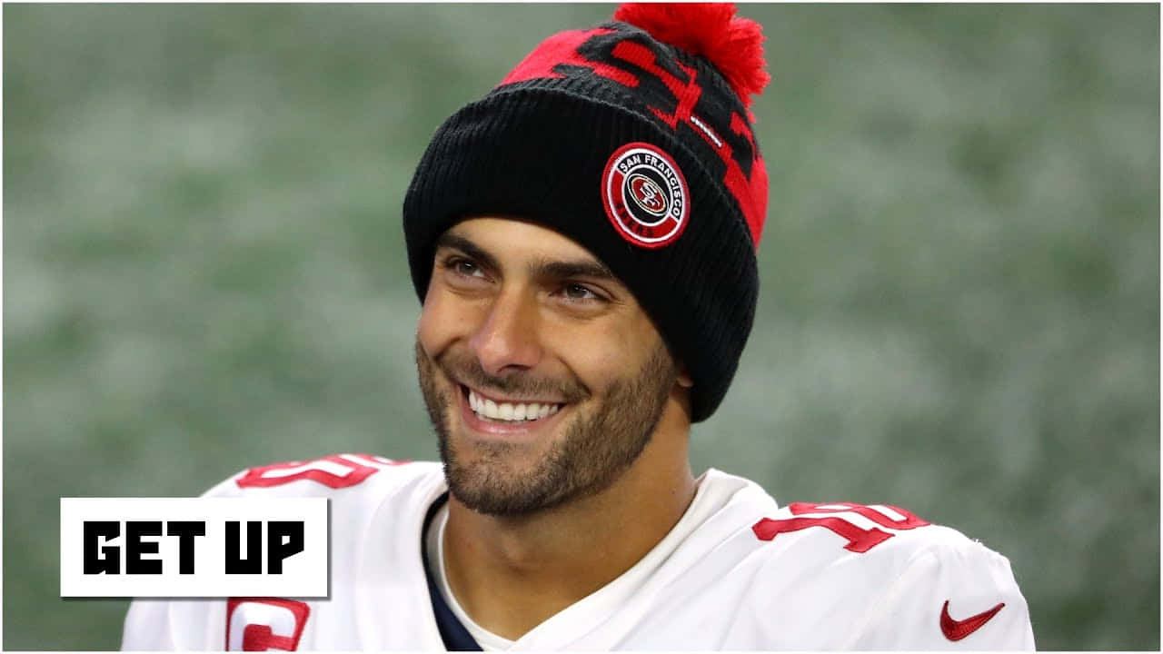 Jimmy Garoppolo 桌布 壁紙 — 一位微笑的美式足球員，戴著三藩市49人隊的冷帽和球衣，帶著燦爛的笑容望向鏡頭外。