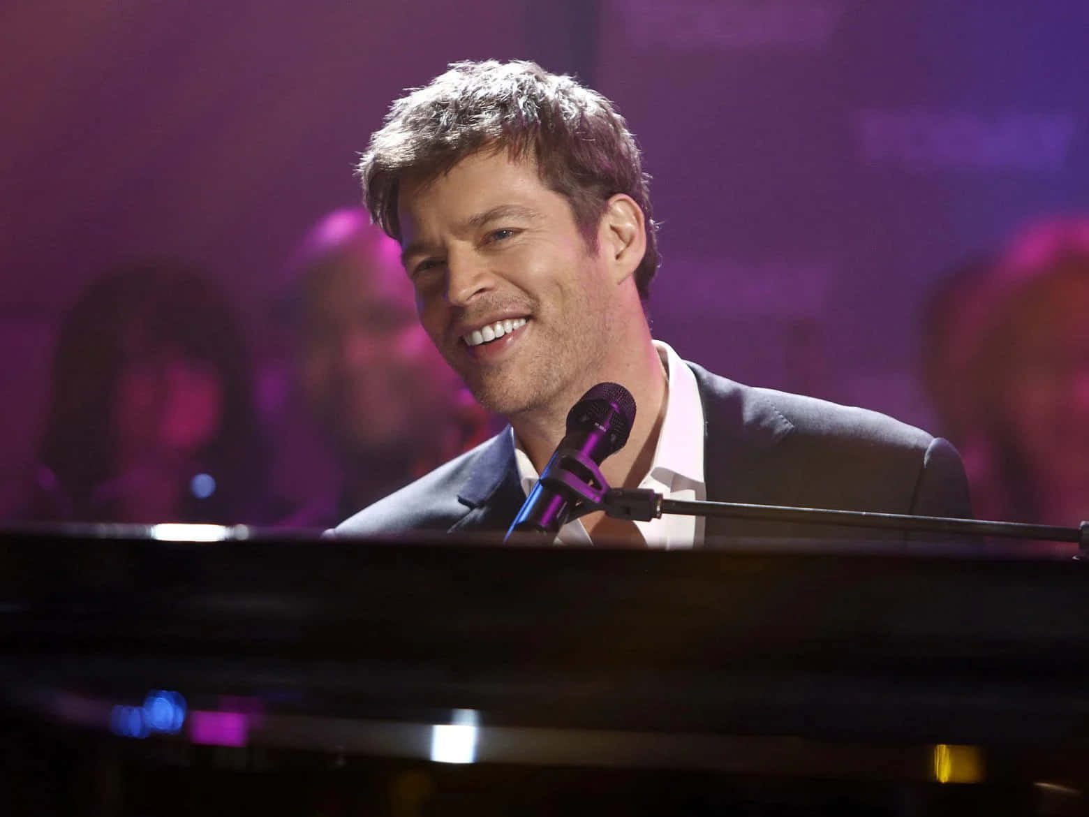 Harry Connick Jr 桌布 壁紙 — 一位微笑的西裝男子在紫色舞台燈光下彈鋼琴，身後有模糊的觀眾。