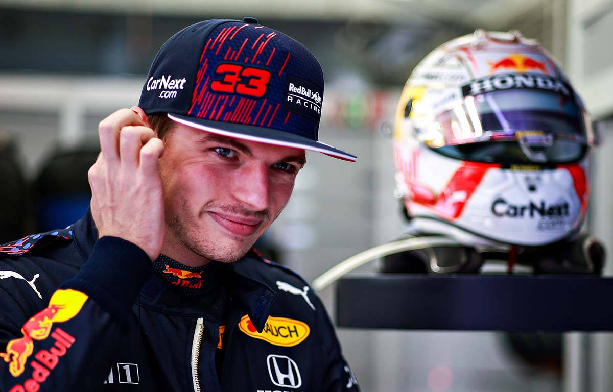 Verstappen 桌布 壁紙 — 一位微笑的賽車手身穿 Red Bull Racing 裝備，在品牌頭盔旁調整帽子。
