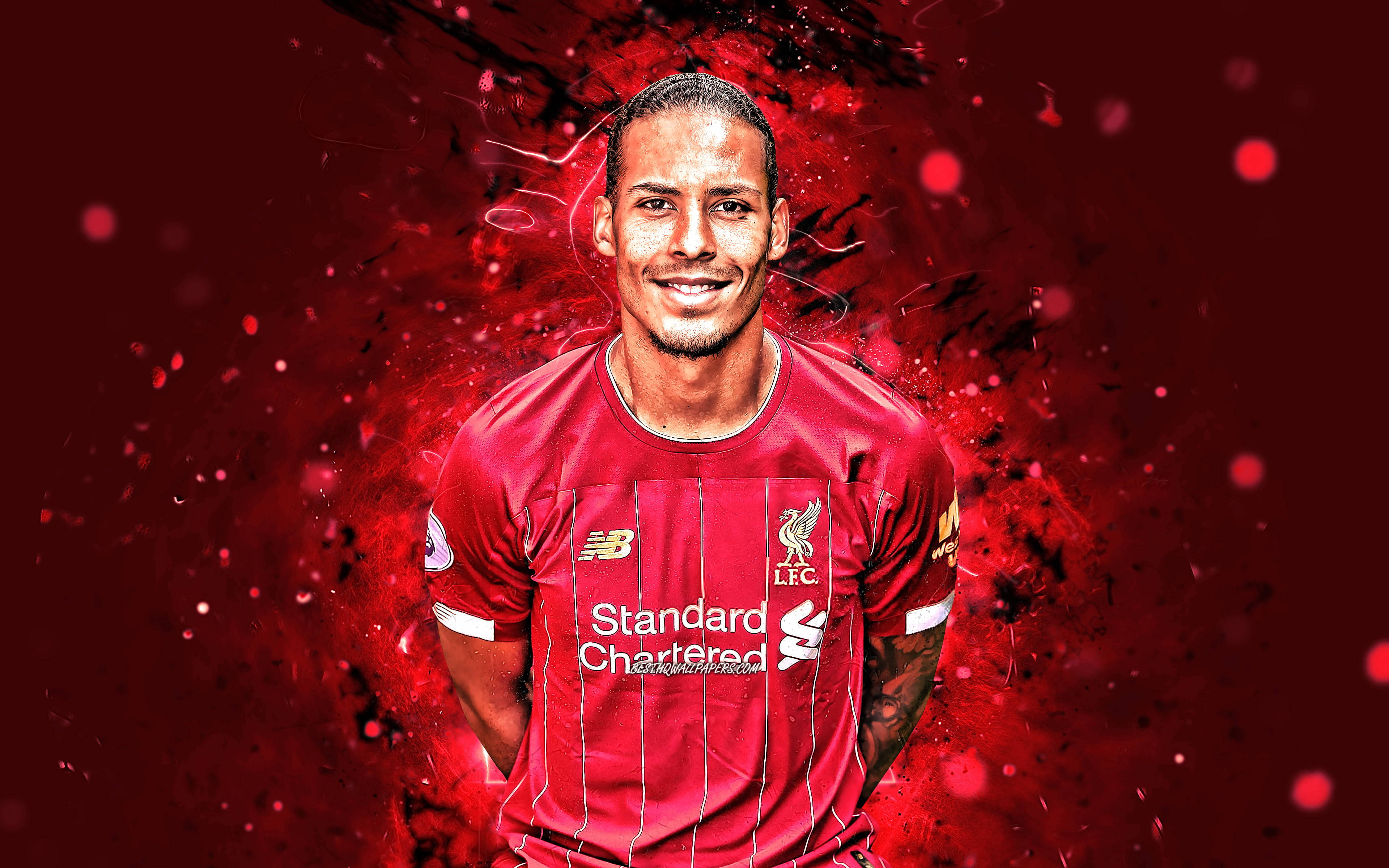 Liverpool Fc 桌布 壁紙 — 一位微笑的足球員身穿紅色利物浦球衣，站在充滿動感的紅色潑濺背景前，伴隨著發光的粒子。