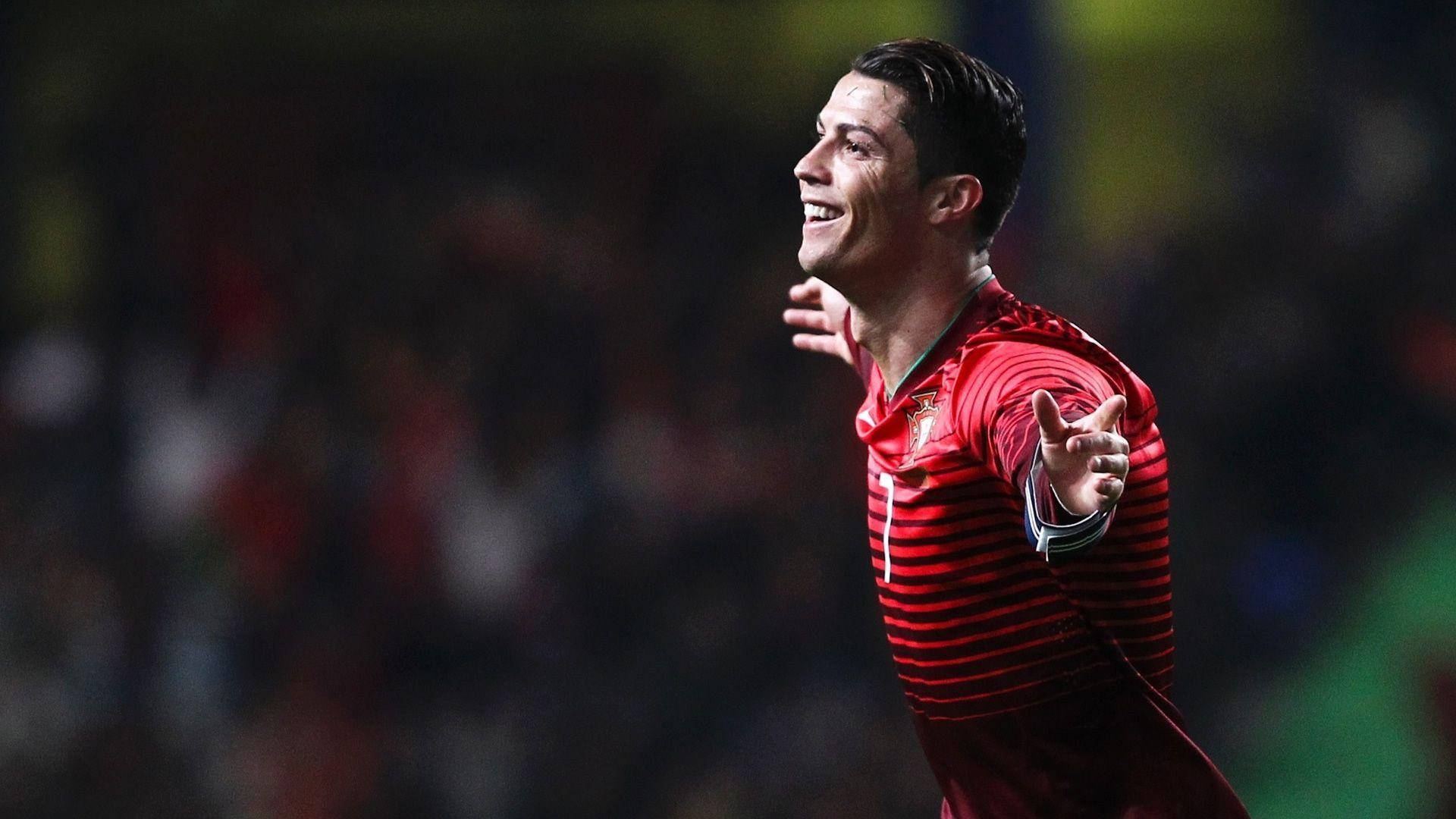 Cristiano Ronaldo 桌布 壁紙 — 一位微笑的足球運動員身穿紅色條紋球衣，在體育場燈光下張開雙臂慶祝。