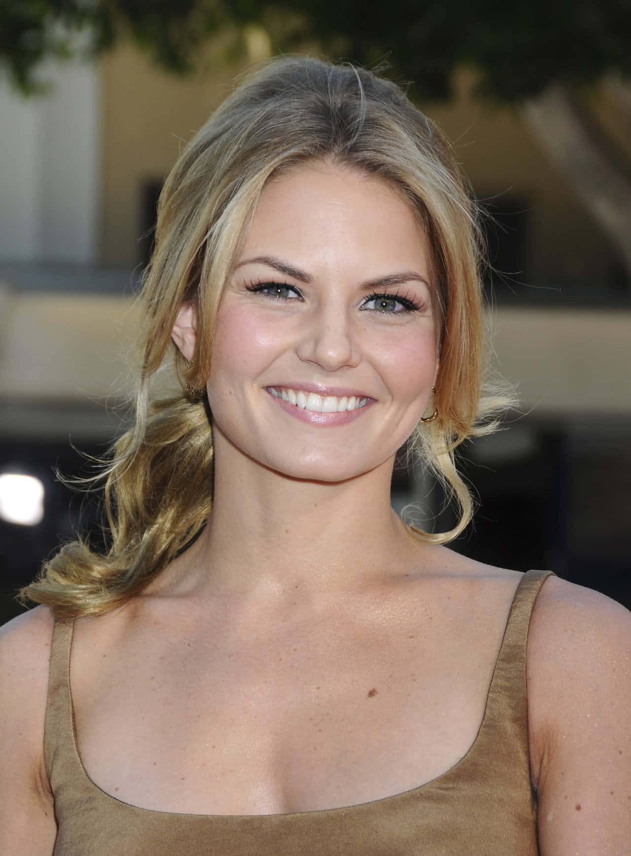 jennifer morrison 桌布 壁紙 — 一位微笑的金髮女性，波浪長髮，明亮雙眸，身穿棕色上衣，背景是柔和模糊的戶外景色。