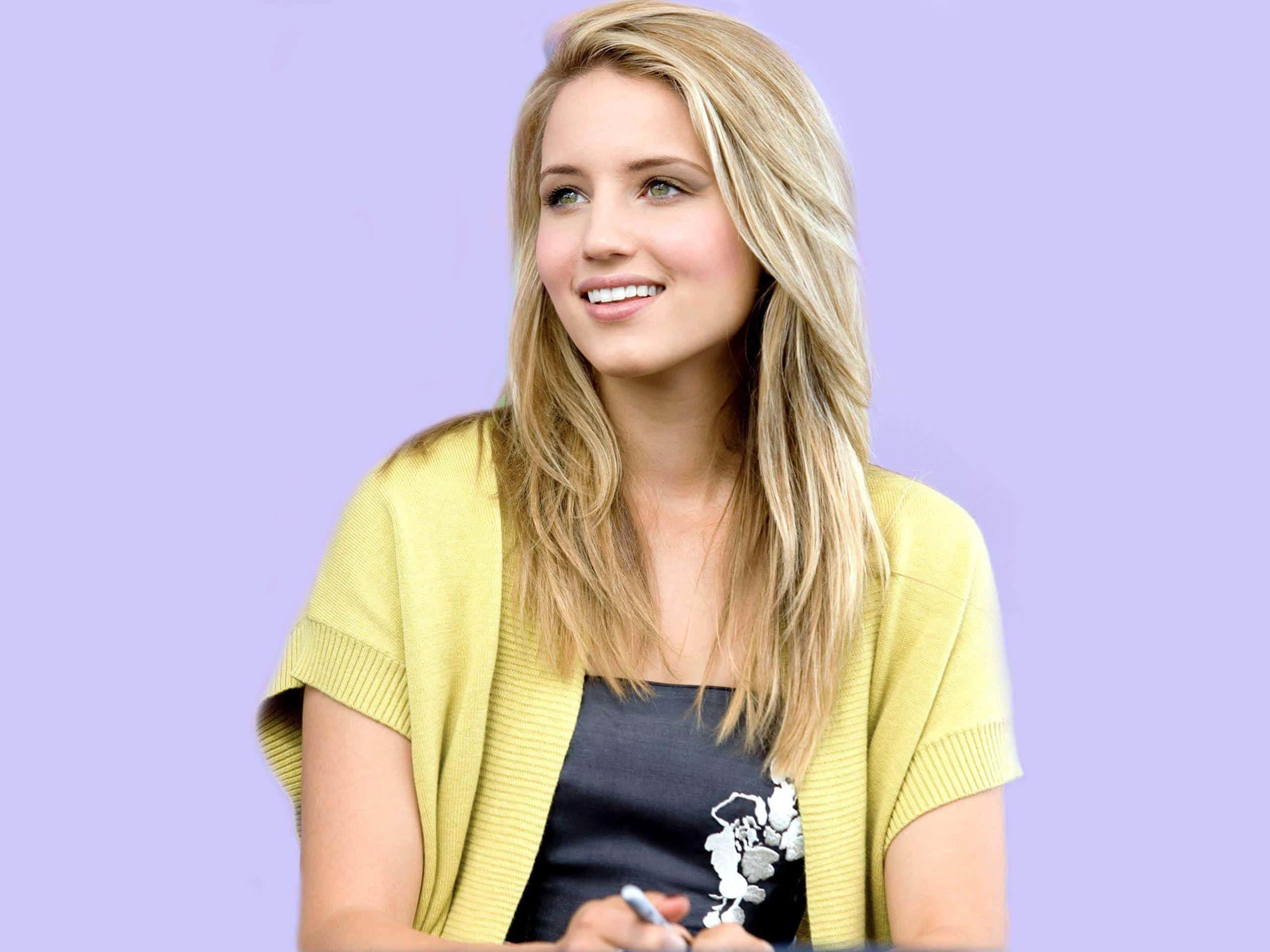 dianna agron 桌布 壁紙 — 一位微笑的金髮女性穿著黃色開襟毛衣，背景是柔和的薰衣草色。