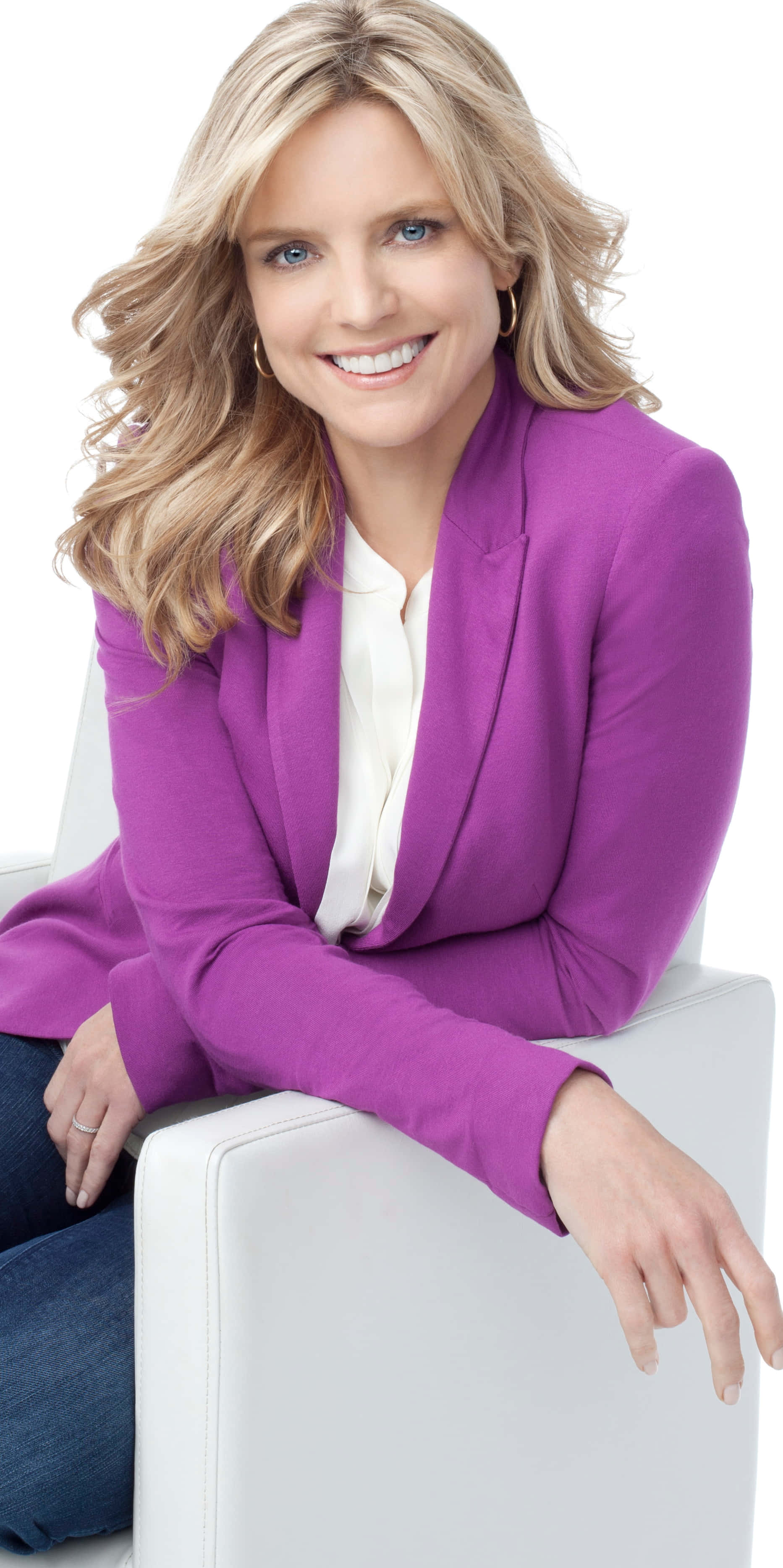 Courtney Thorne Smith 桌布 壁紙 — 一位微笑的金髮女性身穿鮮豔紫色西裝外套，自信地坐在白色椅子上，背景是潔淨的白色。