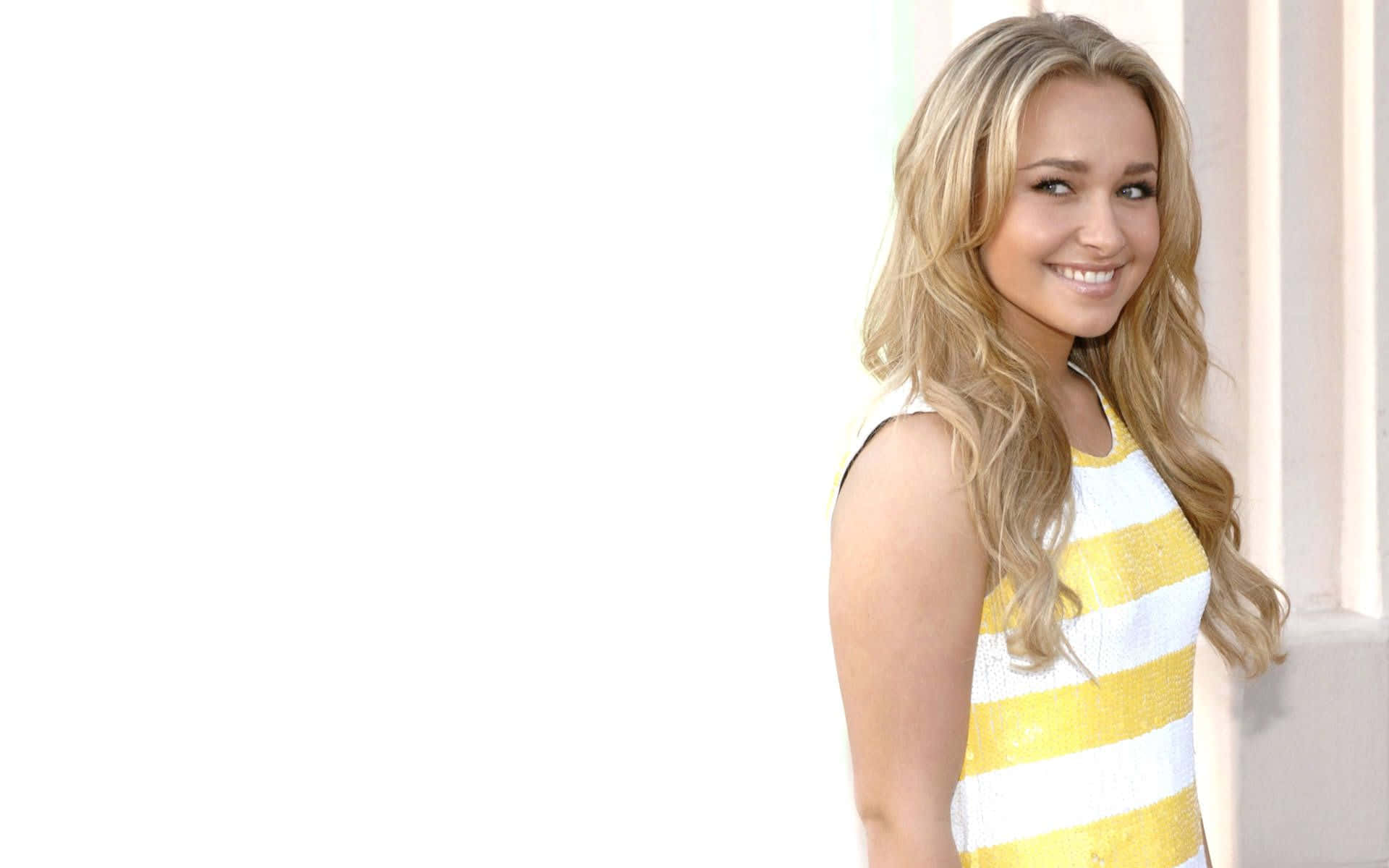 hayden panettiere 桌布 壁紙 — 一位微笑的金髮女性身穿黃白條紋連衣裙，站在明亮的白色背景前。
