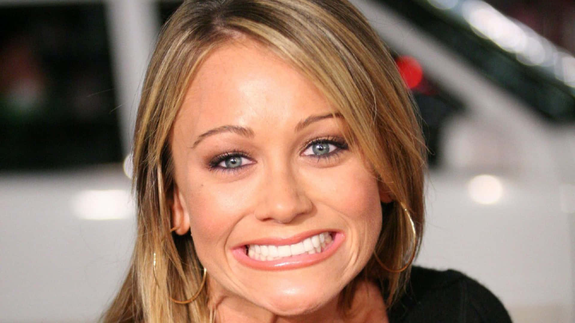 Christine Taylor 桌布 壁紙 — 一位微笑的金髮藍眼女性戴著金色圓環耳環的特寫肖像。