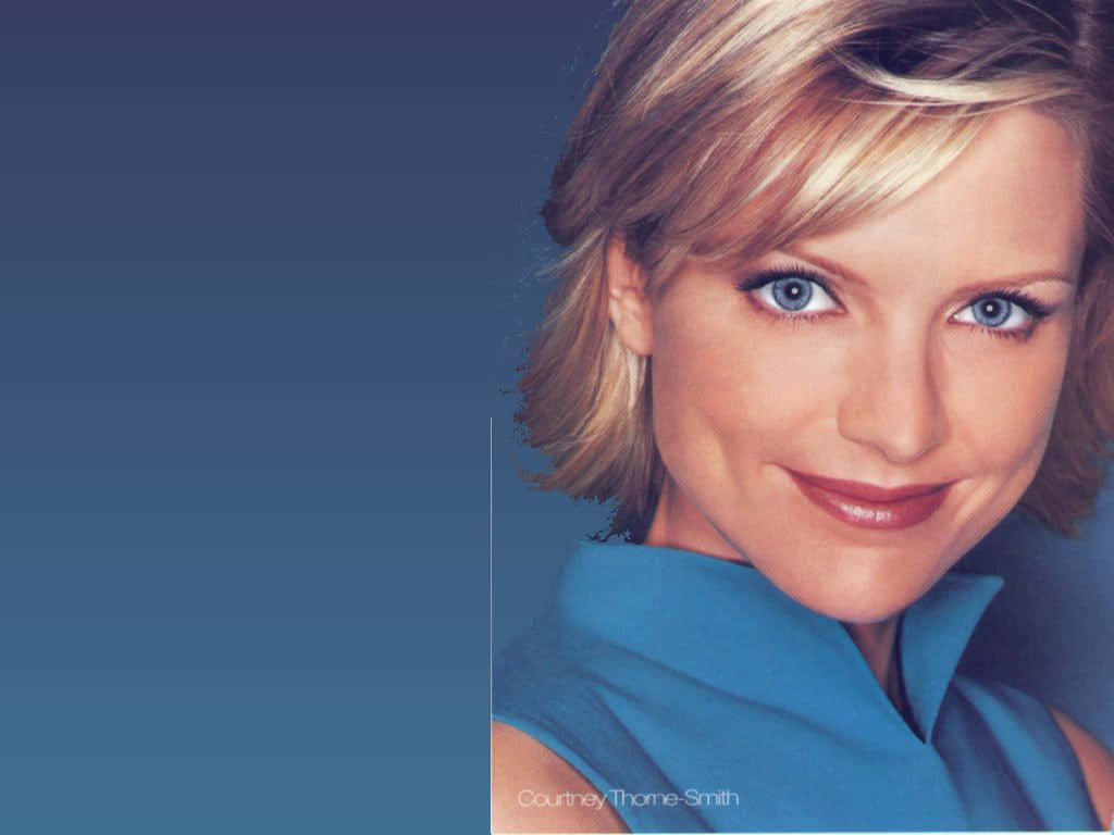 Courtney Thorne Smith 桌布 壁紙 — 一位微笑的金髮藍眼女性穿著藍色上衣，在漸變藍色背景前的特寫肖像。