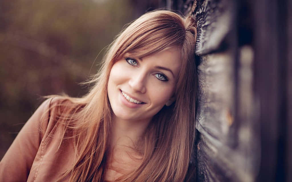 women 桌布 壁紙 — 一位微笑的長金髮女性在柔和自然光中靠著紋理牆壁。