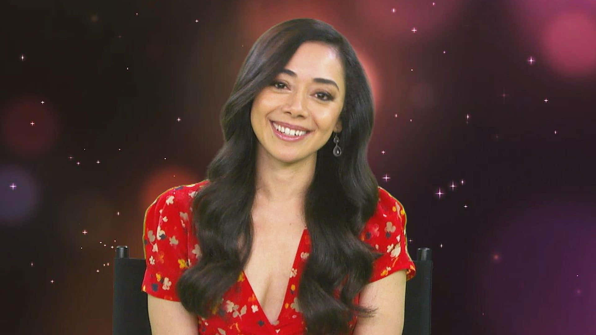 Aimee Garcia 桌布 壁紙 — 一位微笑的長黑髮女性，穿著紅色花卉連衣裙，背景是閃爍的紫色散景。