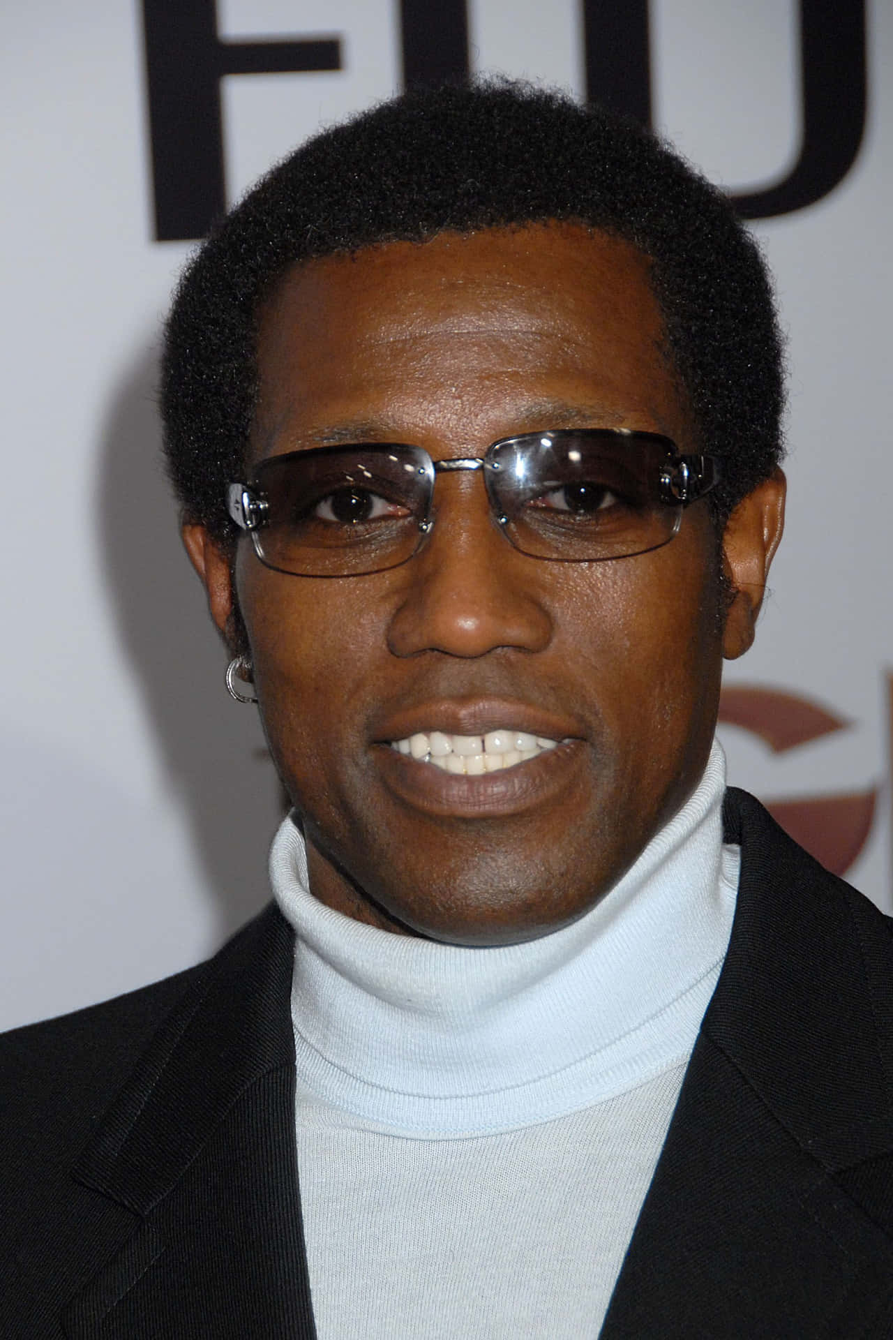 Wesley Snipes 桌布 壁紙 — 一位微笑的黑人男士近距離肖像，戴著時尚太陽眼鏡，黑色西裝外套內搭白色高領毛衣。