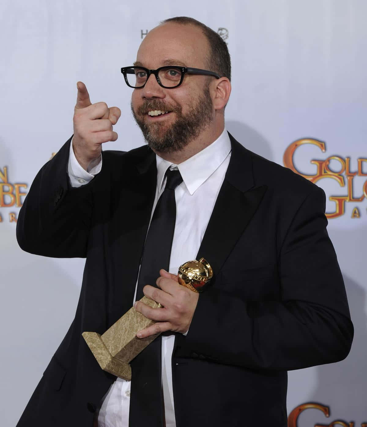 Paul Giamatti 桌布 壁紙 — 一位微笑的黑西裝眼鏡男士在紅地毯上手持金色獎盃並指向鏡頭。