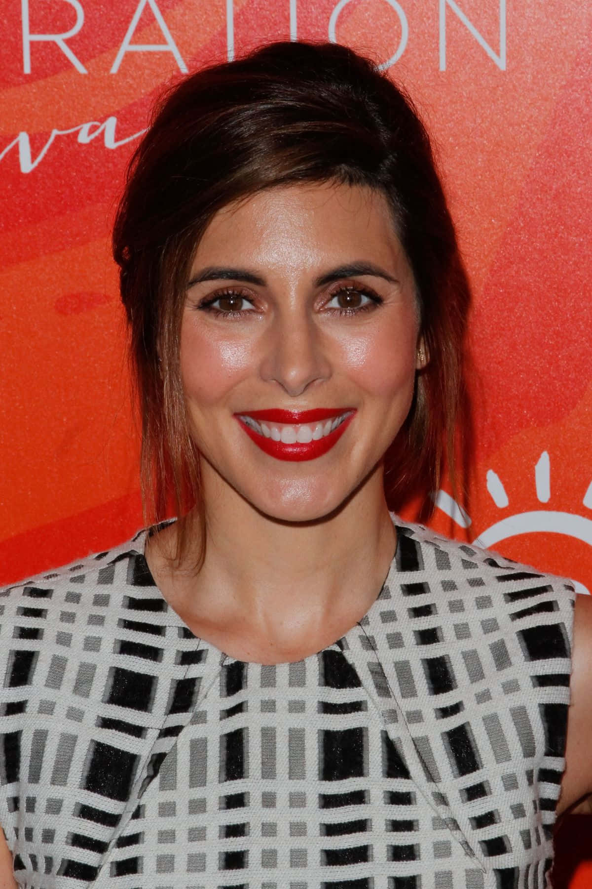 Jamie Lynn Sigler 桌布 壁紙 — 一位微笑的黑髮女性塗著大膽的紅色唇膏，穿著黑白幾何圖案連衣裙，背景是鮮豔的橙色。
