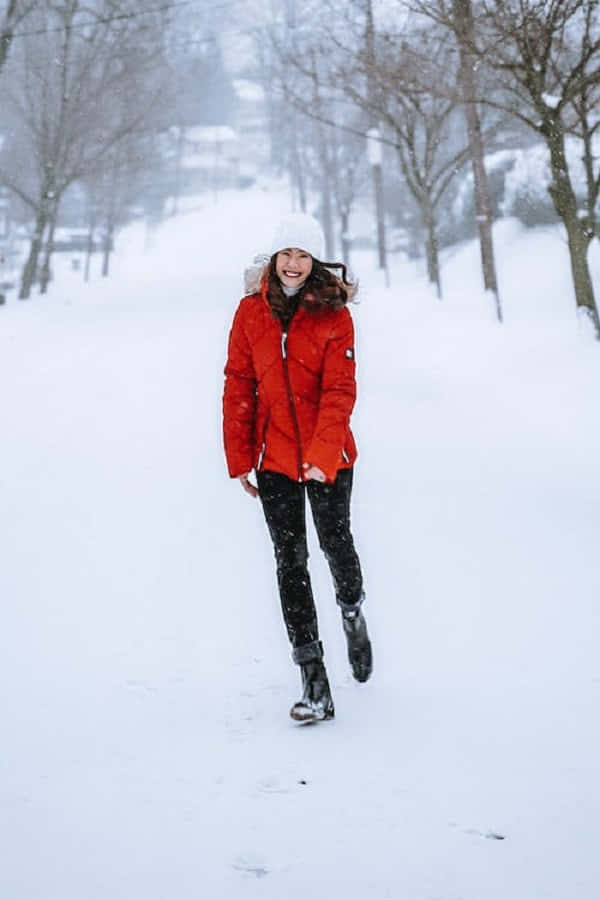 Snowshoes 桌布 壁紙 — 一位快樂的女人穿著鮮紅色冬季外套和白色無邊帽，在一個有裸樹和飄落雪花的雪地公園裡跳躍。