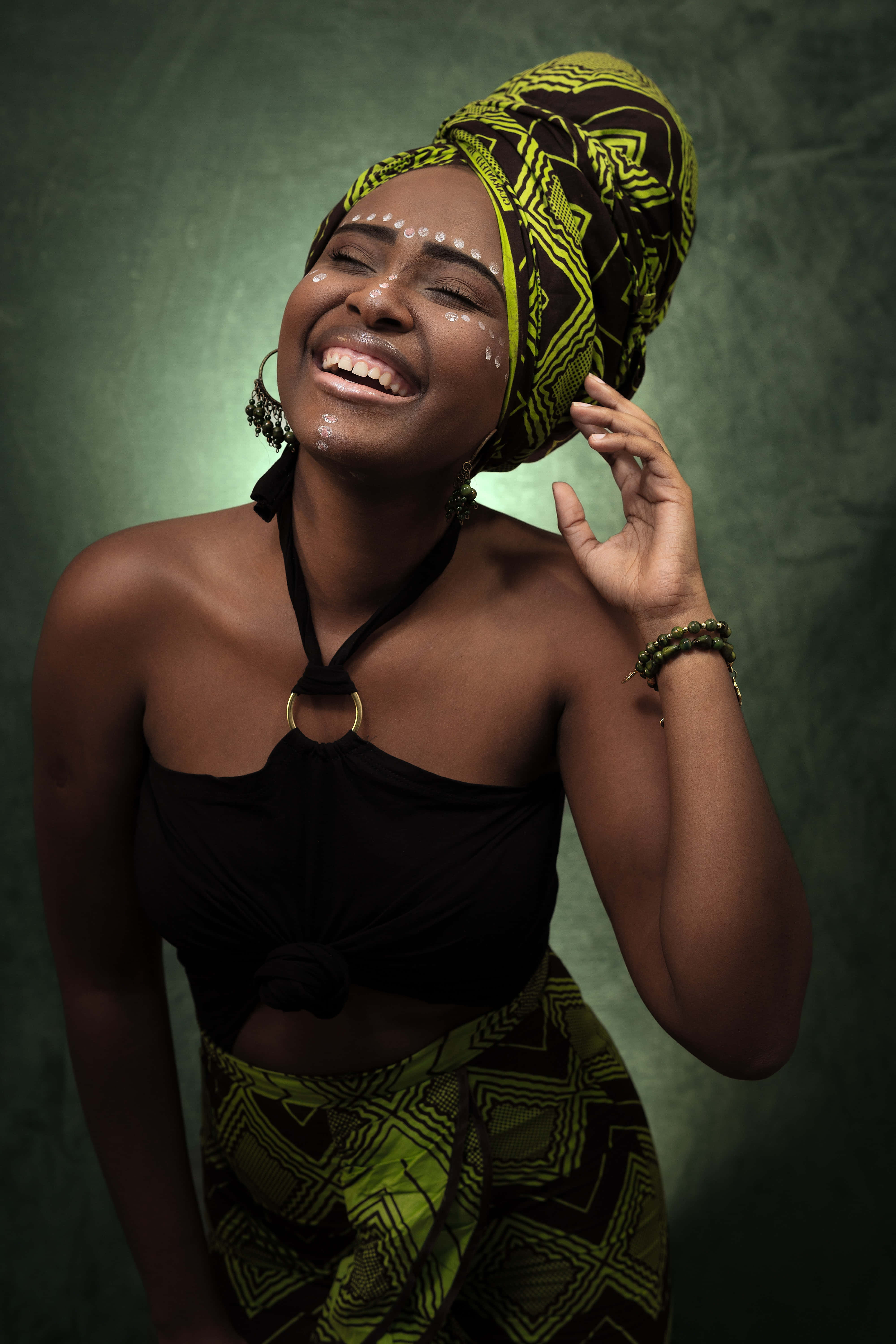 African 桌布 壁紙 — 一位快樂的女性，戴著充滿活力的綠色和黑色圖案頭巾，在紋理綠色背景前閉眼大笑。