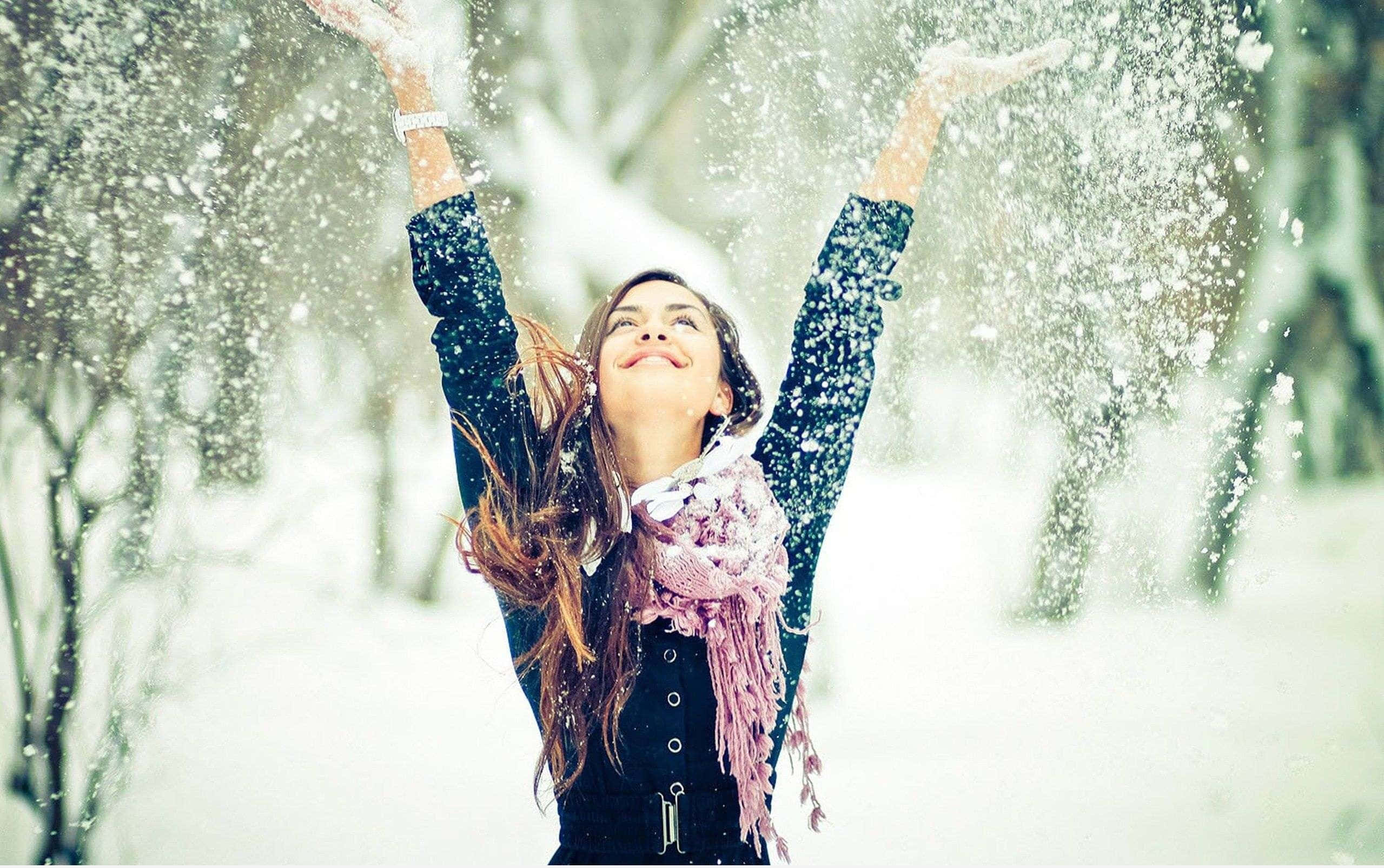 Winter Fashion 桌布 壁紙 — 一位快樂的女性在白雪皚皚的冬季森林中高舉雙臂將雪拋向空中。
