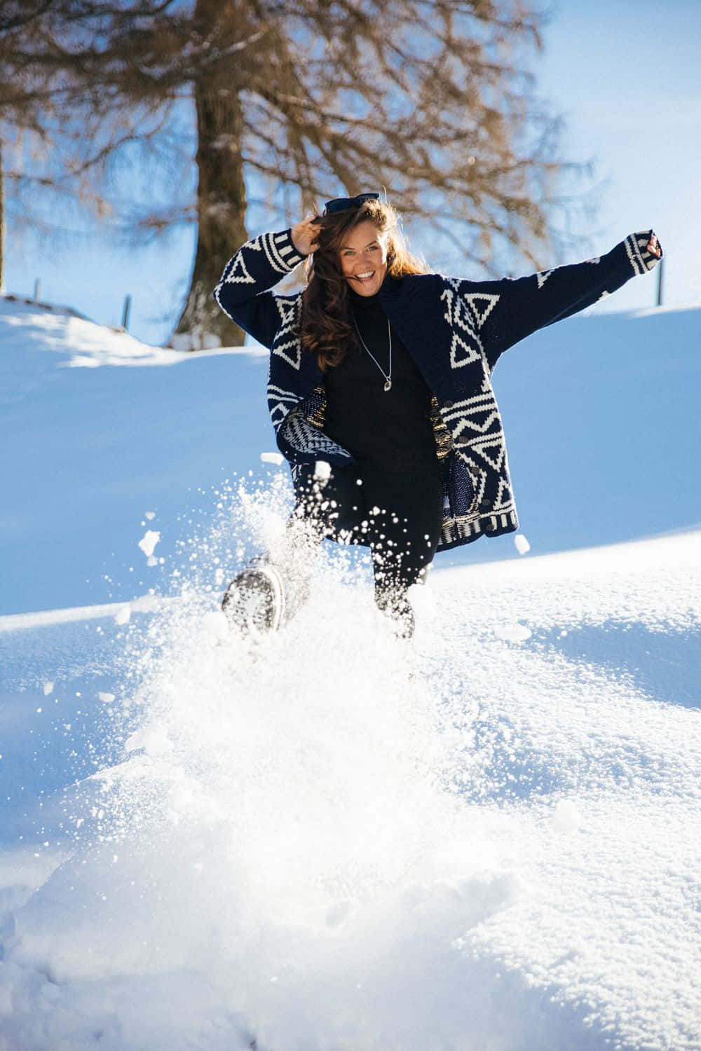 Winter Photography 桌布 壁紙 — 一位快樂的女性身穿圖案海軍藍外套，在晴朗藍天下張開雙臂跳過新雪。