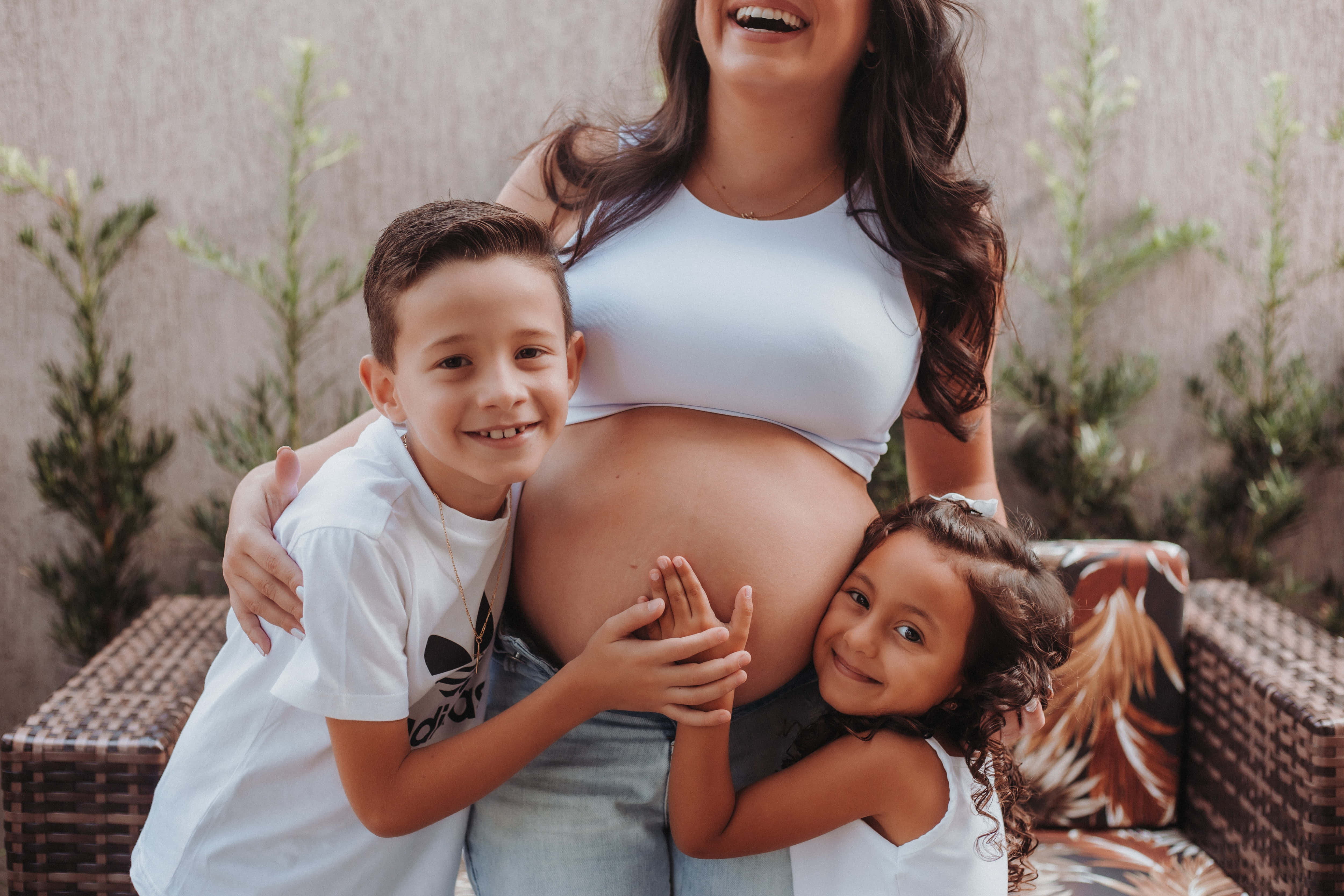 Mom 桌布 壁紙 — 一位快樂的孕婦與兩個微笑的孩子在戶外親切地擁抱她的肚子，開懷大笑。