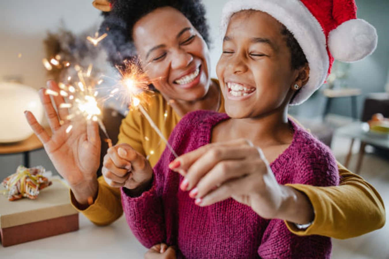 New Years Eve 桌布 壁紙 — 一位快樂的母親和女兒在室內節日慶祝活動中一起笑著拿著煙花棒。