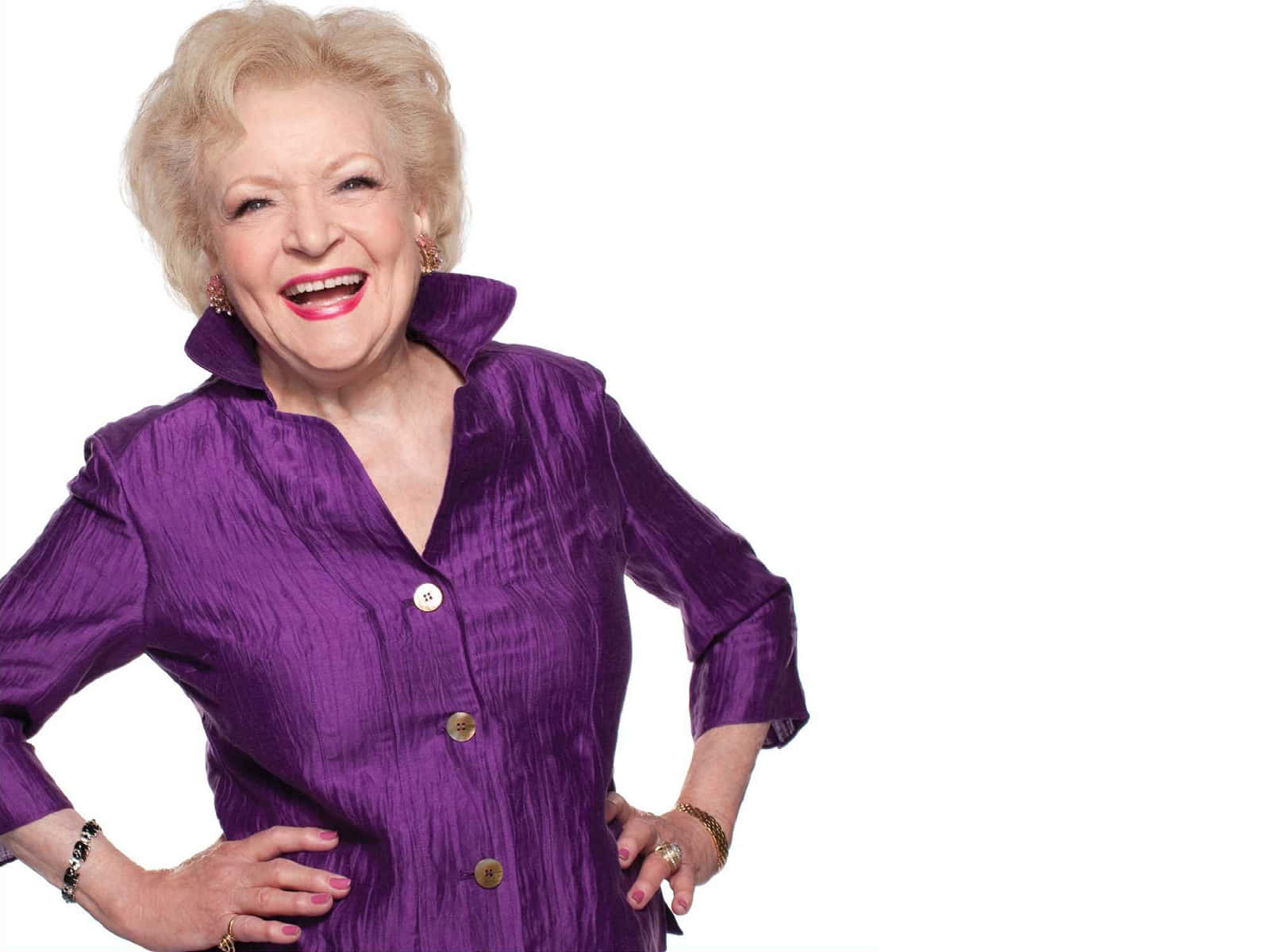Betty White 桌布 壁紙 — 一位快樂的老年女士穿著鮮豔的紫色襯衫，在純白背景前開懷大笑。