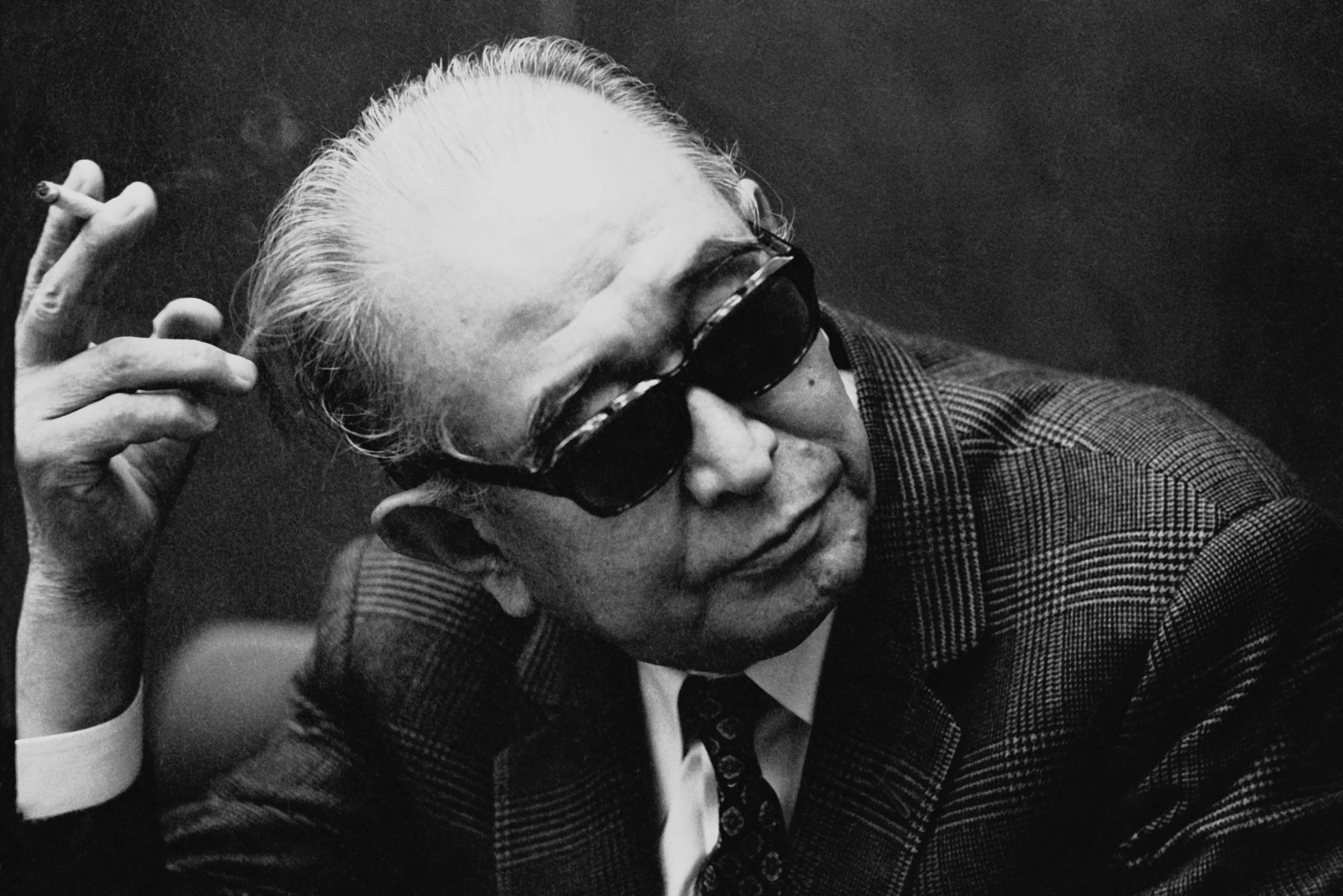 Akira Kurosawa 桌布 壁紙 — 一位戴太陽眼鏡的長者手持香煙的黑白肖像，表情沉思。