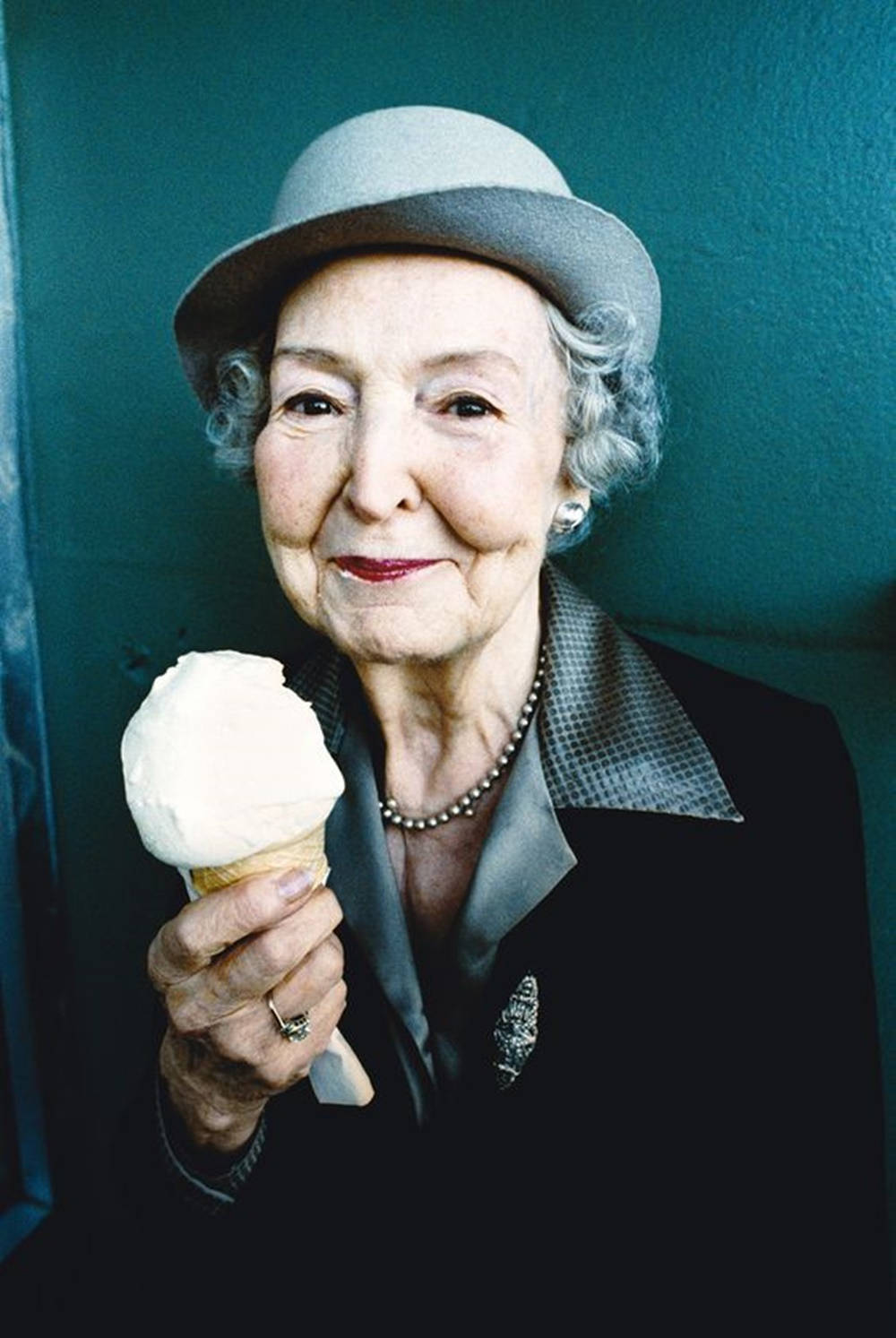 Grandma 桌布 壁紙 — 一位戴灰色帽子的老婦人，在青綠色牆壁前拿著一個雲呢拿雪糕筒，露出溫暖的笑容。