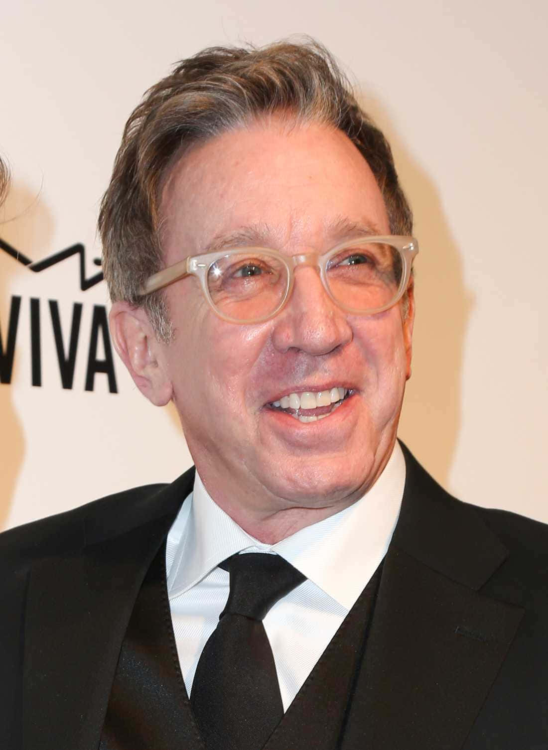 Tim Allen 桌布 壁紙 — 一位戴眼鏡、灰白頭髮的微笑男士，身穿黑色西裝和領帶，背景為白色，帶有部分文字。