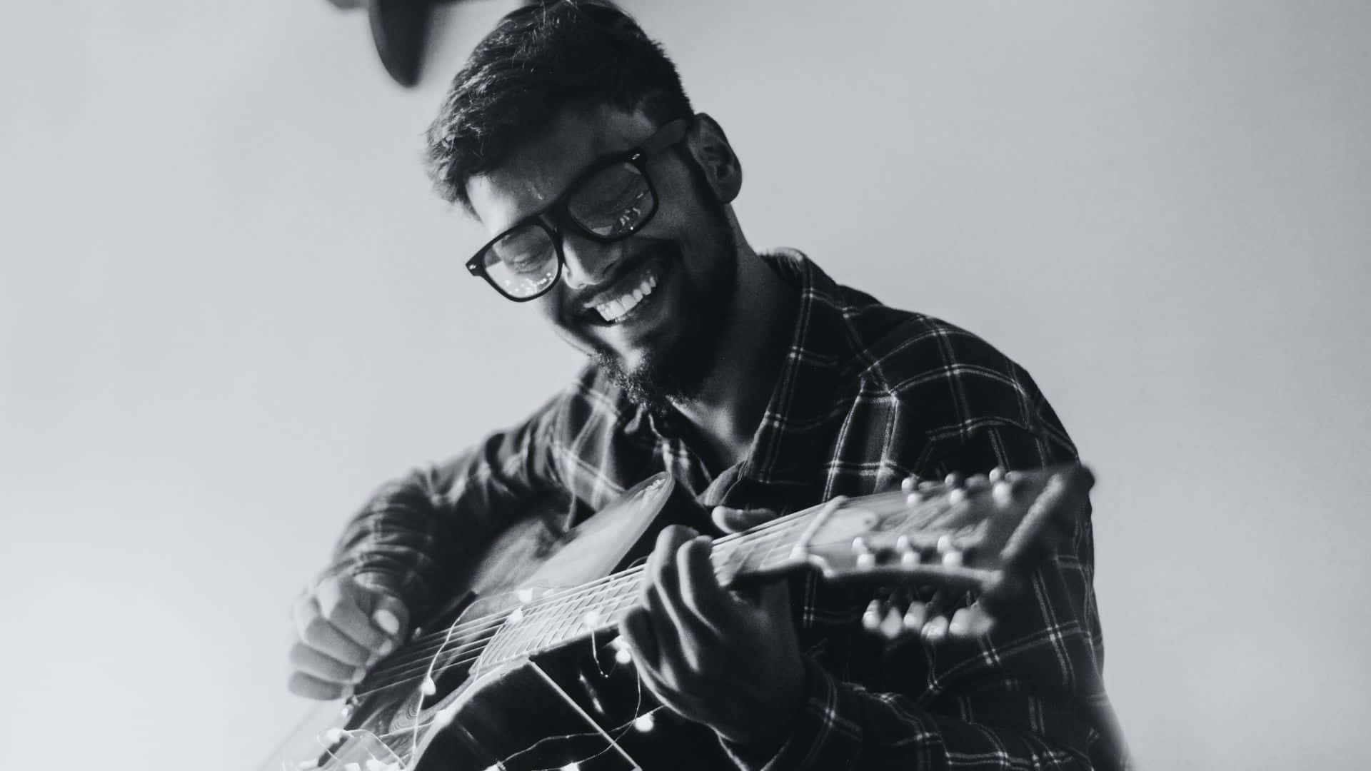 Black And White Guitar 桌布 壁紙 — 一位戴眼鏡、留鬍子的快樂男士，在黑白工作室照中微笑彈奏木結他。