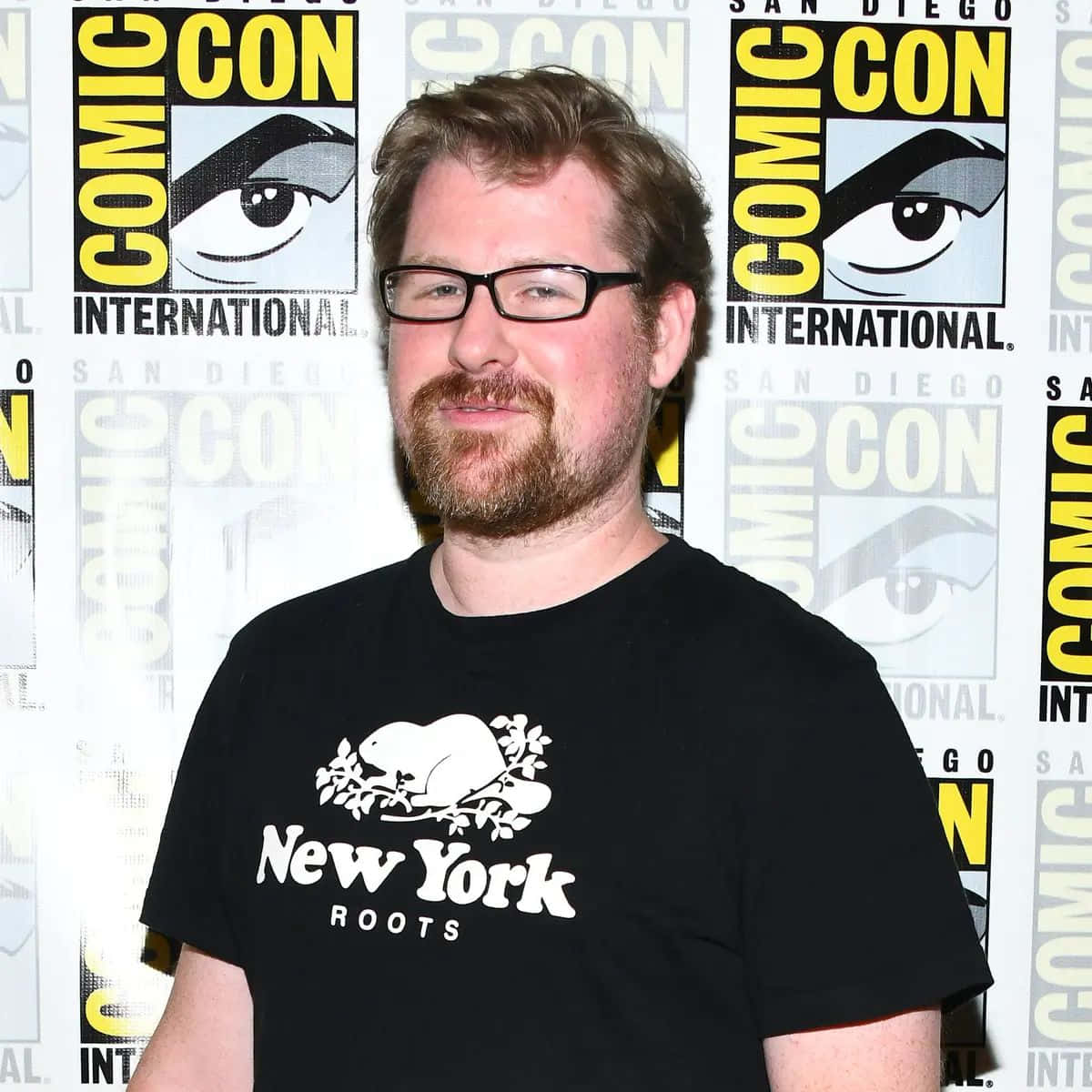 Justin Roiland 桌布 壁紙 — 一位戴眼鏡、留鬍鬚的男人在Comic-Con活動中穿著印有海狸圖案的黑色T恤對著鏡頭微笑。