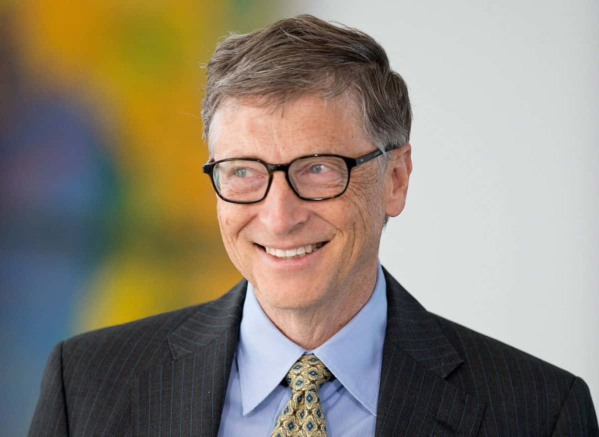 Bill Gates 桌布 壁紙 — 一位戴眼鏡微笑的男子，穿著細條紋西裝和圖案領帶，背景是色彩繽紛的模糊效果。