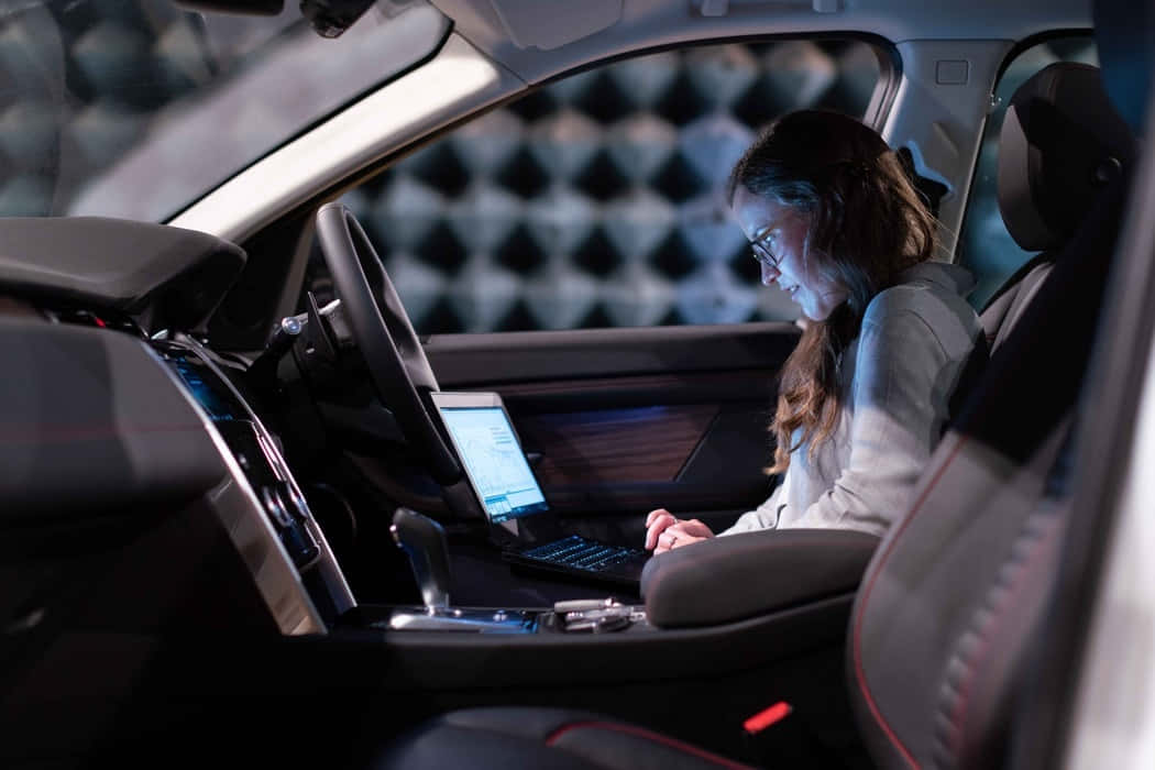 Car Technology 桌布 壁紙 — 一位戴眼鏡的女性在夜間於現代汽車內，在環境燈光下使用手提電腦工作。