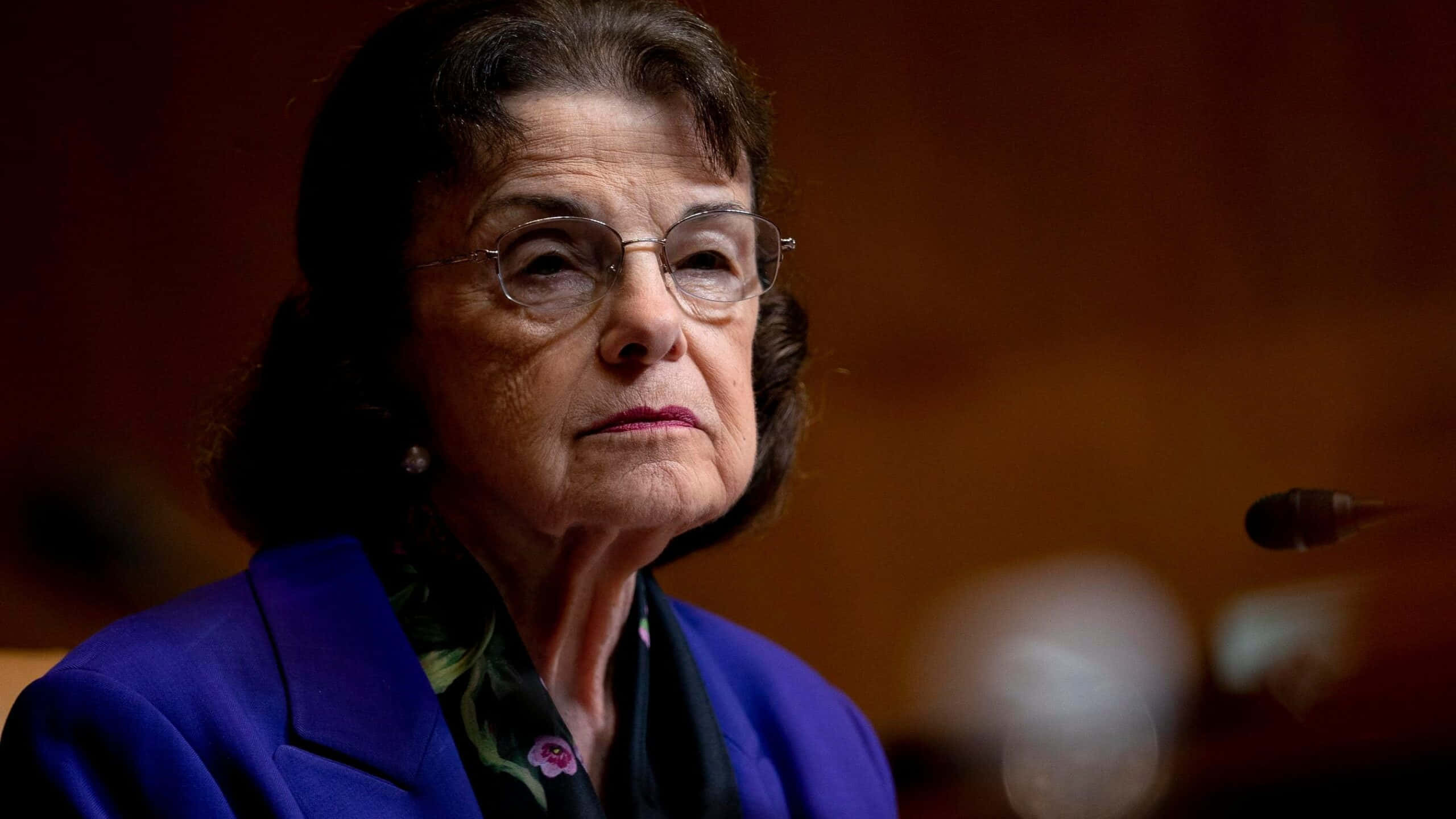 Dianne Feinstein 桌布 壁紙 — 一位戴眼鏡的老年女士在正式場合穿著鮮藍色西裝外套和花卉圍巾的 close-up 肖像。