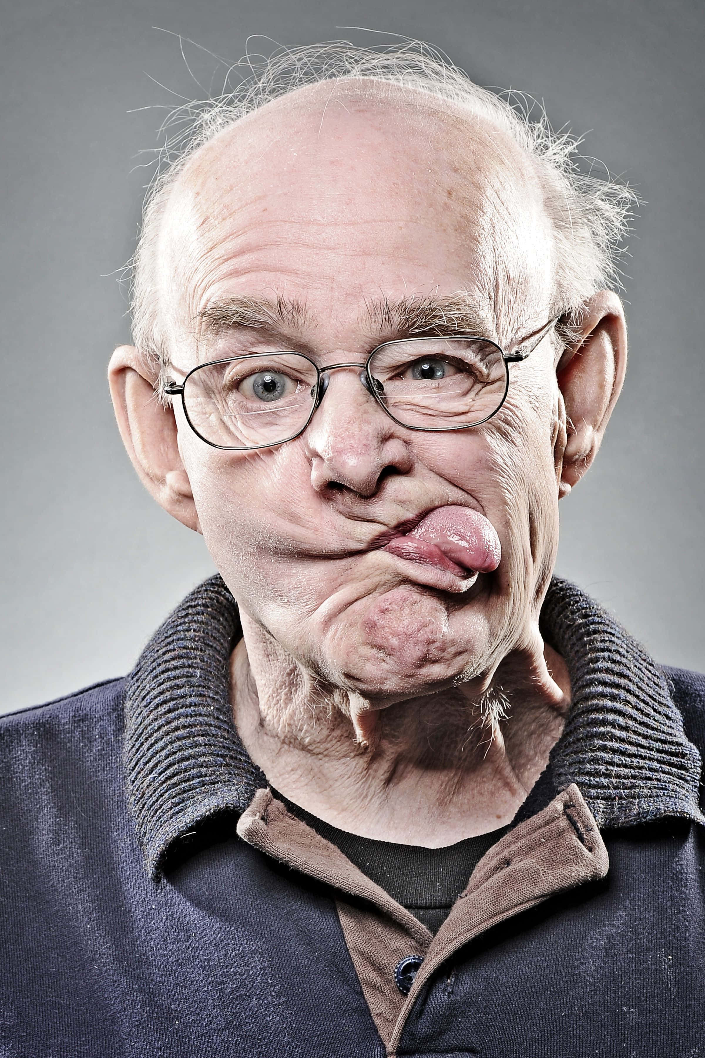 Funny Faces 桌布 壁紙 — 一位戴眼鏡的長者對著純灰色背景頑皮地伸出舌頭。