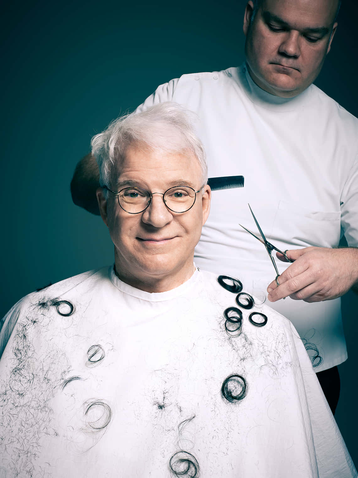 steve martin 桌布 壁紙 — 一位戴眼鏡的長者微笑著，理髮師在青綠色背景前修剪他的白髮。
