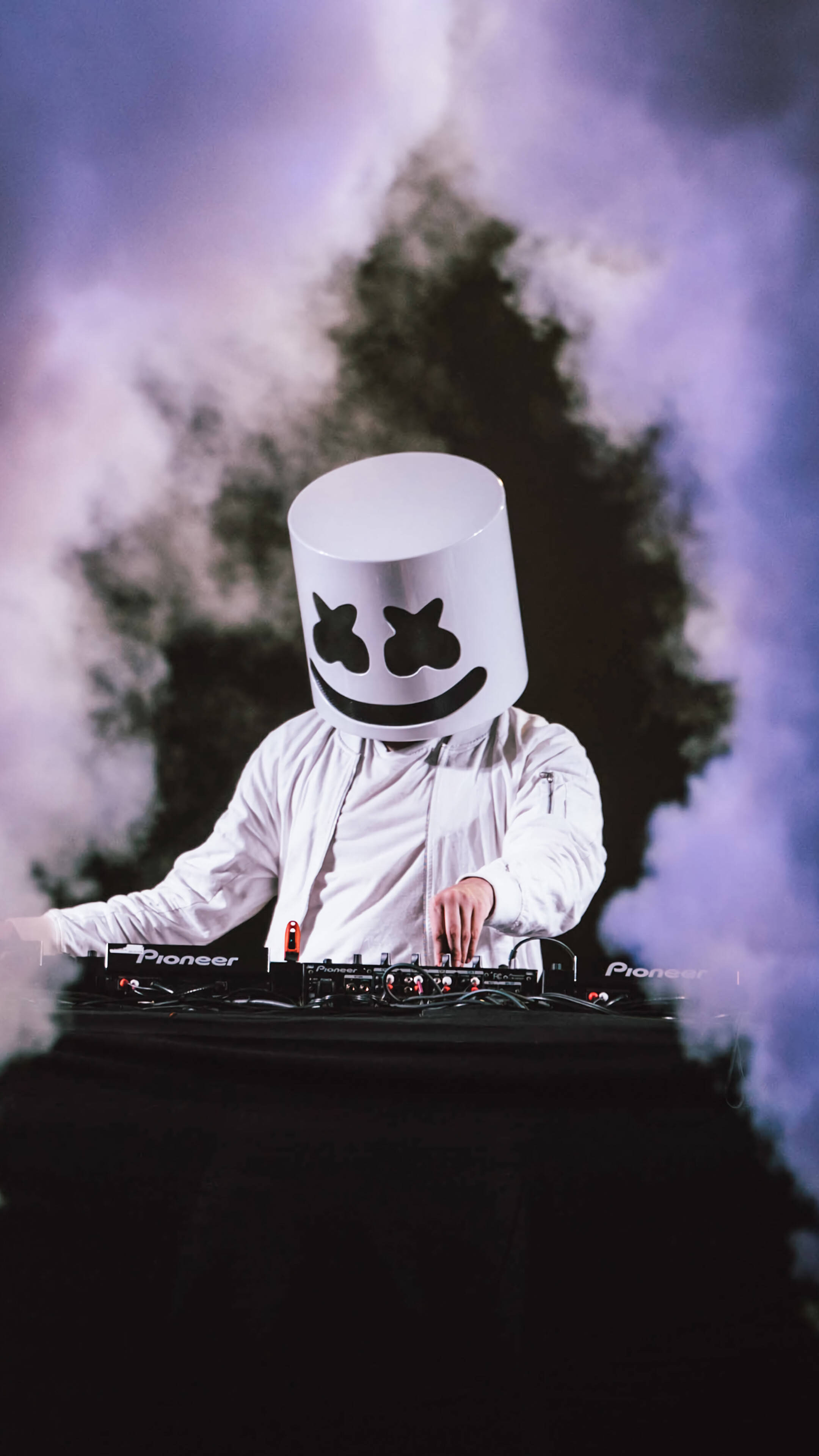 marshmello iPhone 桌布 壁紙 — 一位戴着白色棉花糖頭盔的DJ在黑暗背景下，於旋轉的紫色煙霧中操作唱盤。