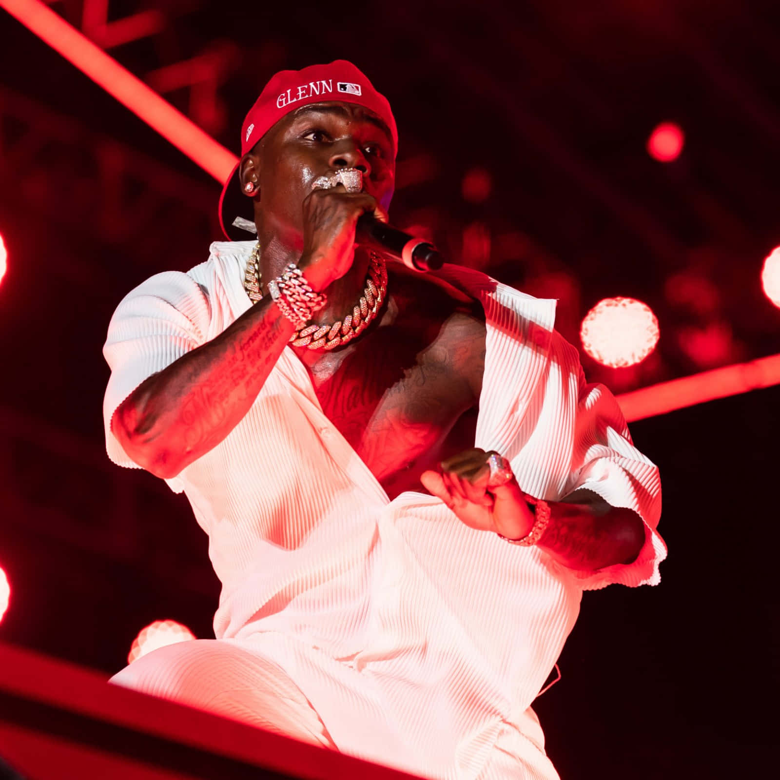Dababy 桌布 壁紙 — 一位戴紅色帽、穿白色服裝的饒舌歌手在強烈的紅色舞台燈光下熱情表演。