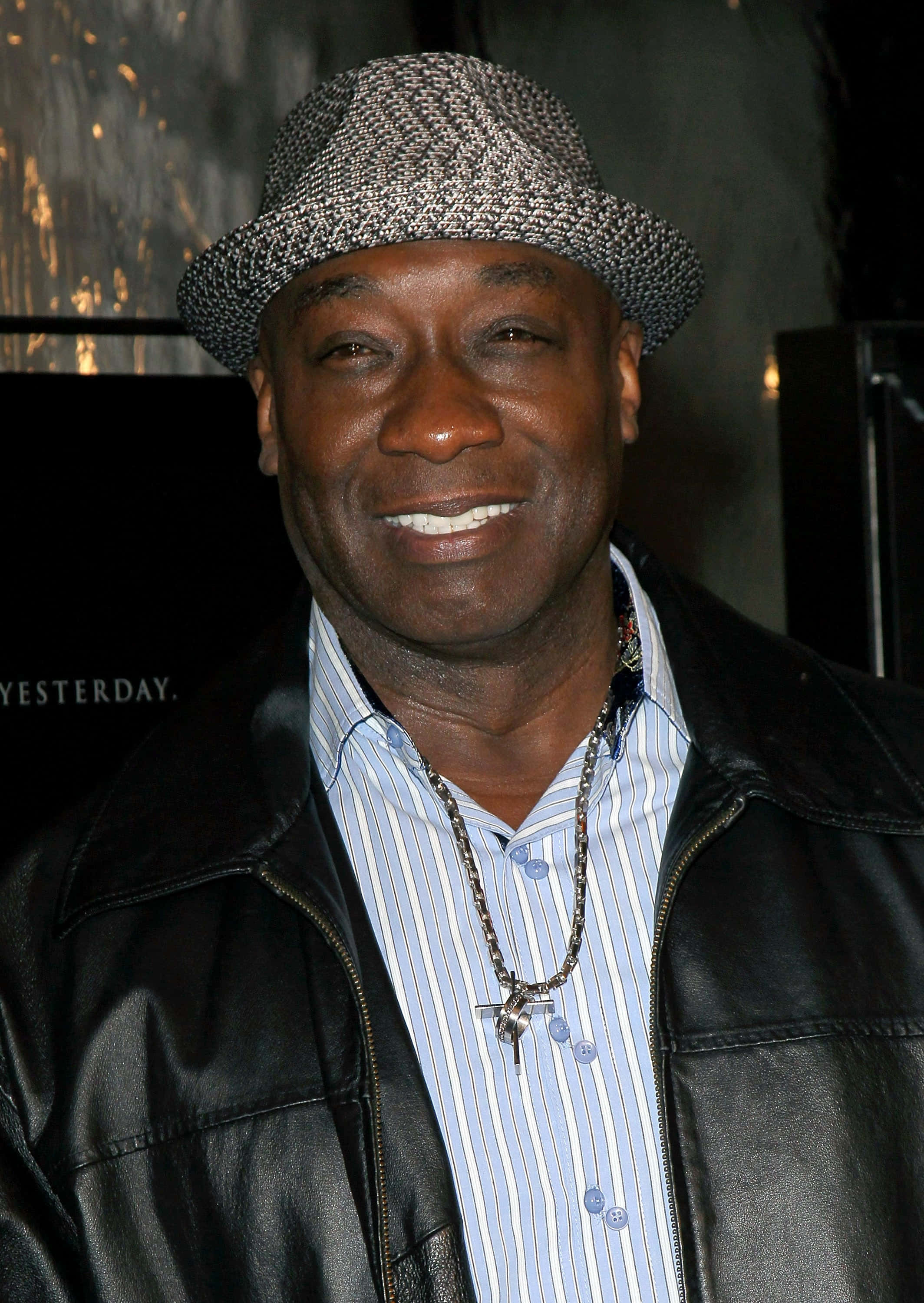 Michael Clarke Duncan 桌布 壁紙 — 一位戴著圖案帽子、皮褸和條紋恤衫的 smiling 男士在活動中自信地擺姿勢。