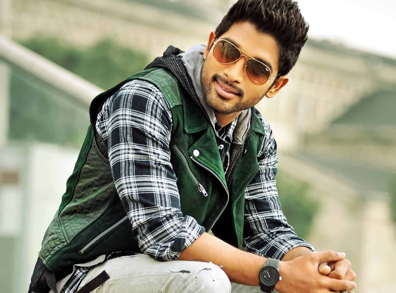 Allu Arjun 桌布 壁紙 — 一位戴著太陽眼鏡和格仔恤衫的時尚男士，在模糊的城市背景下自信地在戶外擺姿勢。