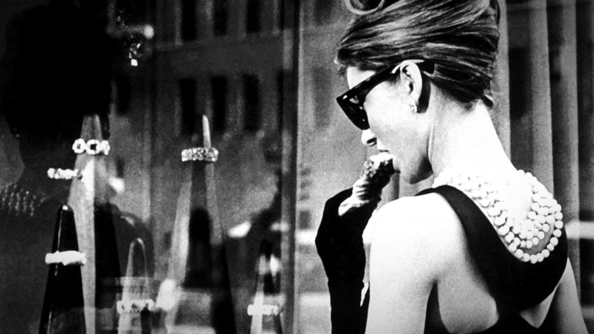 Black And White Film 桌布 壁紙 — 一位戴著太陽眼鏡和珍珠項鍊的女性，一邊吃著冰淇淋甜筒，一邊看著珠寶店的櫥窗。