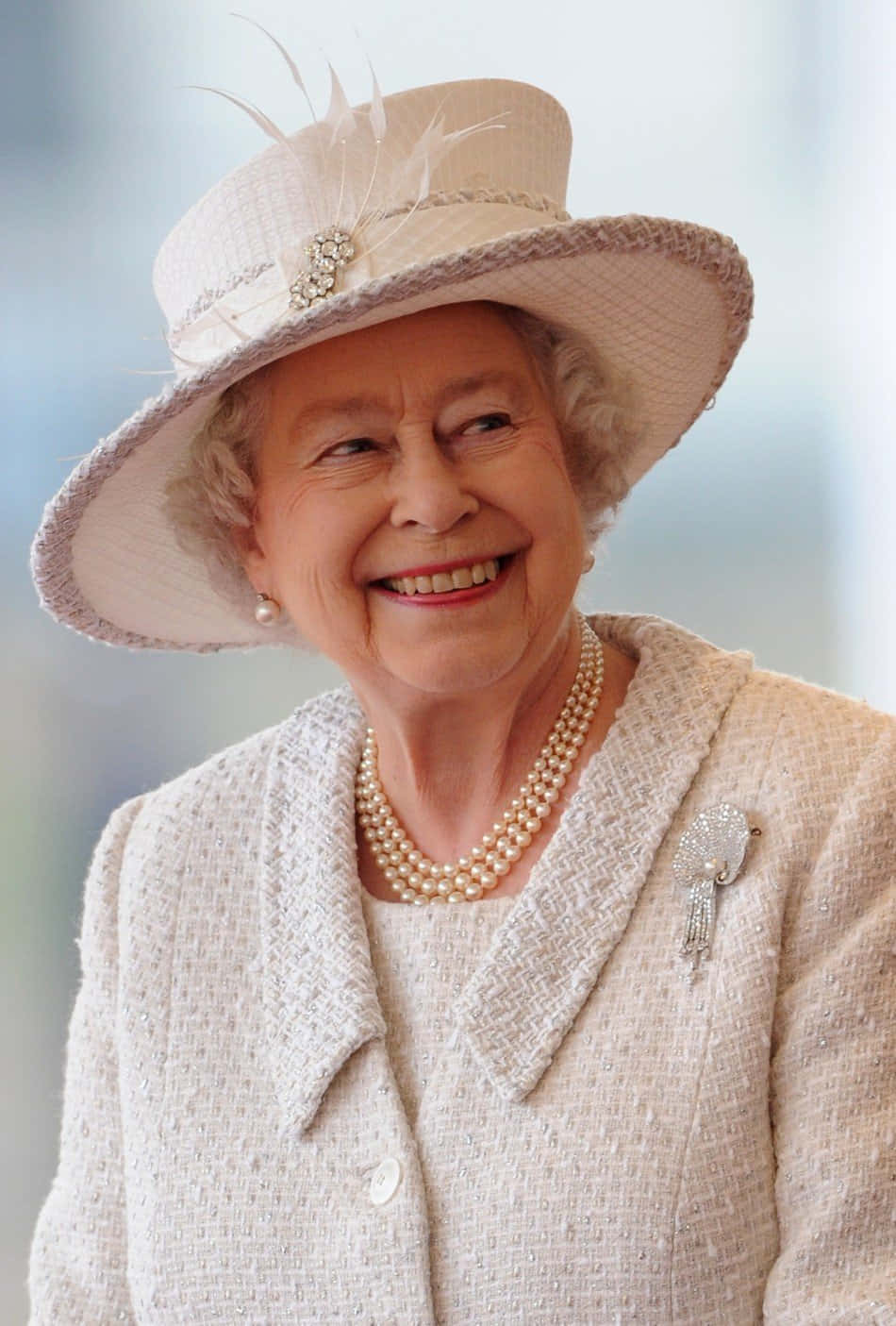 Queen Elizabeth 桌布 壁紙 — 一位戴著奶油色帽子和珍珠的耀眼老年女性，在柔和模糊的背景中溫暖地微笑。