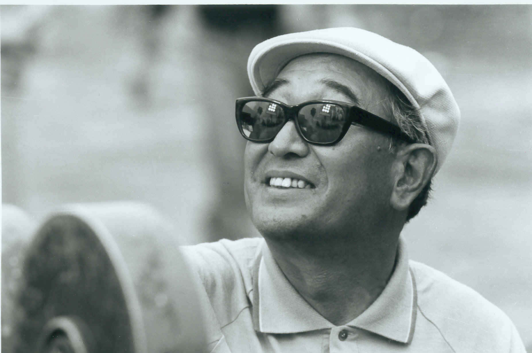 Akira Kurosawa 桌布 壁紙 — 一位戴著帽子和太陽眼鏡的開朗長者，在健身房舉重時微笑。