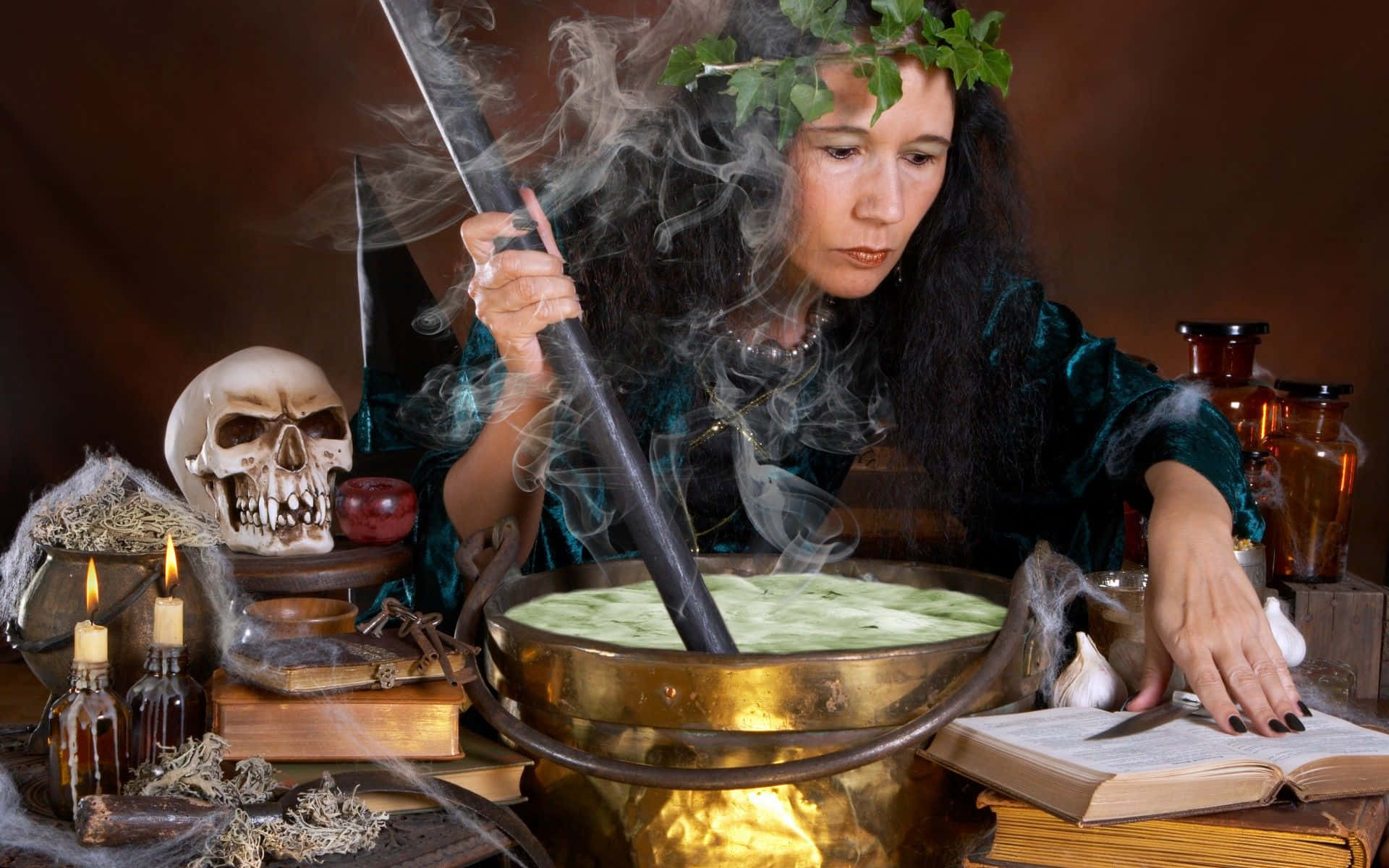 cauldron 桌布 壁紙 — 一位戴著樹葉皇冠的女巫在一個被頭骨、蠟燭和古籍包圍的黃銅大鍋中攪拌冒著蒸汽的綠色藥水。